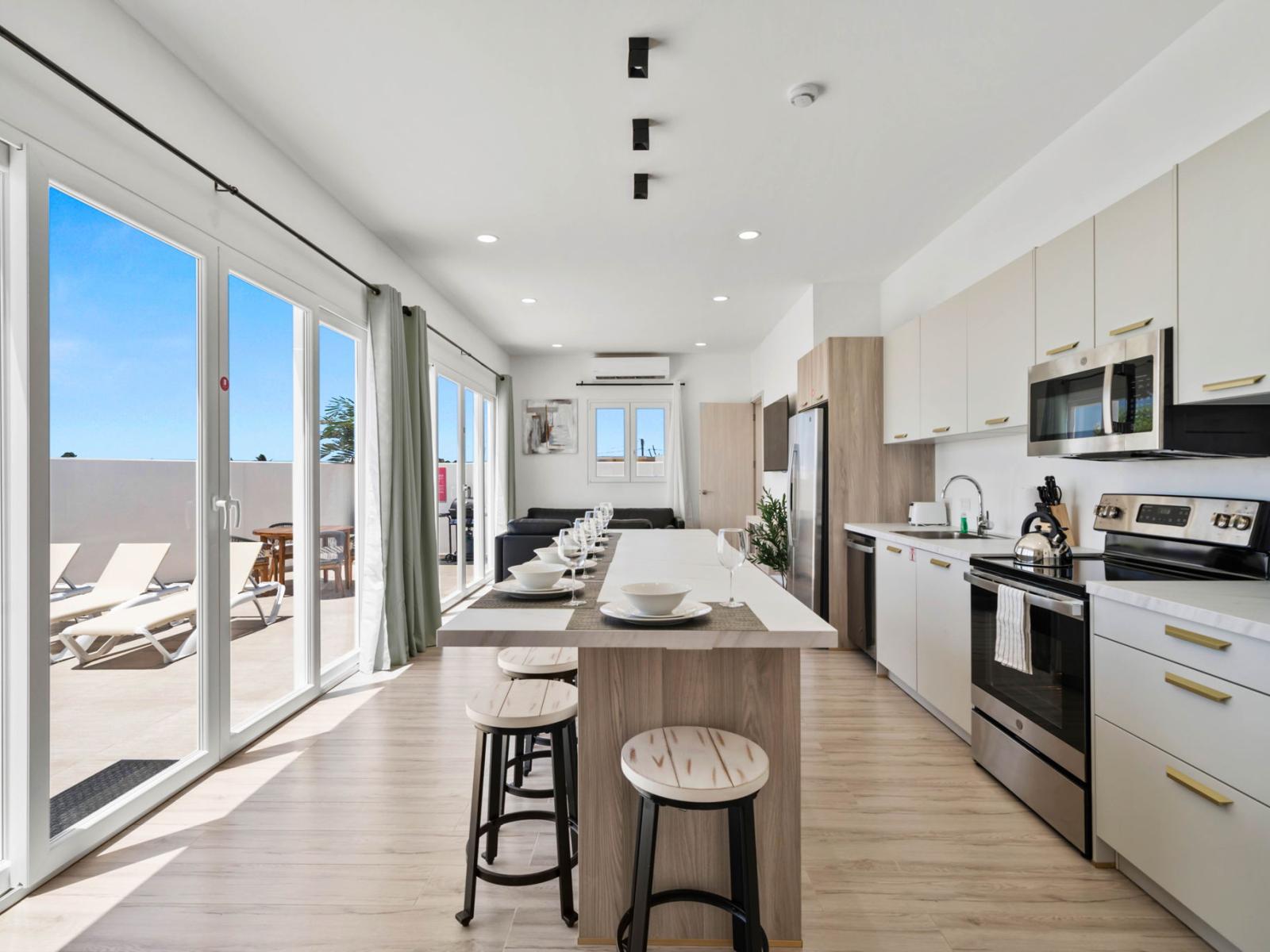 - Spacious kitchen with modern appliances and an island bar, perfect for meal prep and casual dining - Glass doors offer a seamless transition to the outdoor lounging area with sunbeds - Bright, open layout ideal for entertaining and relaxation