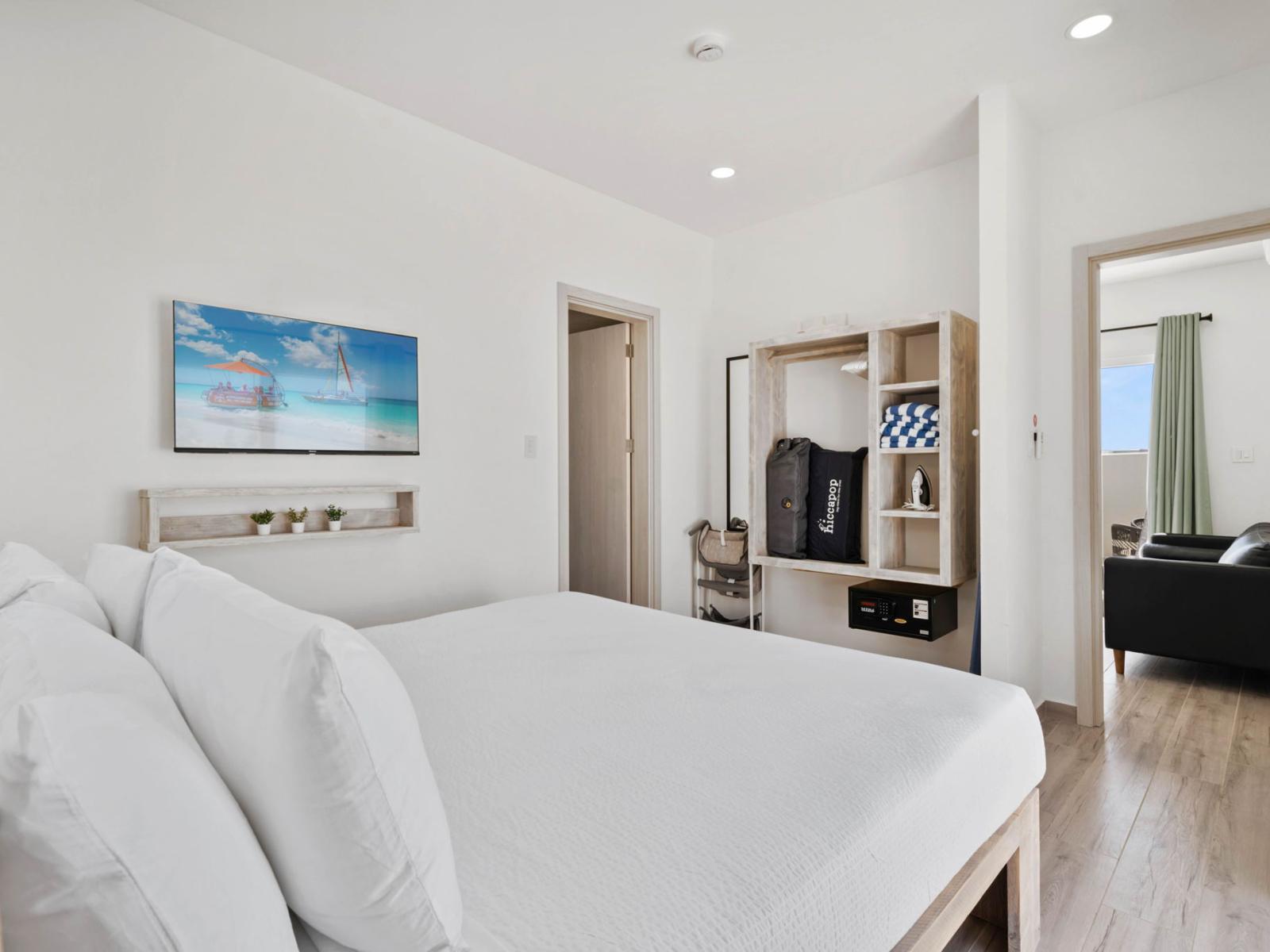 - Comfortable bedroom with a simple yet stylish design, featuring a cozy bed with fresh white linen - Open shelving and wardrobe provide storage space, including a safe for valuables - Wall-mounted TV and minimalist decor create a relaxing atmosphere