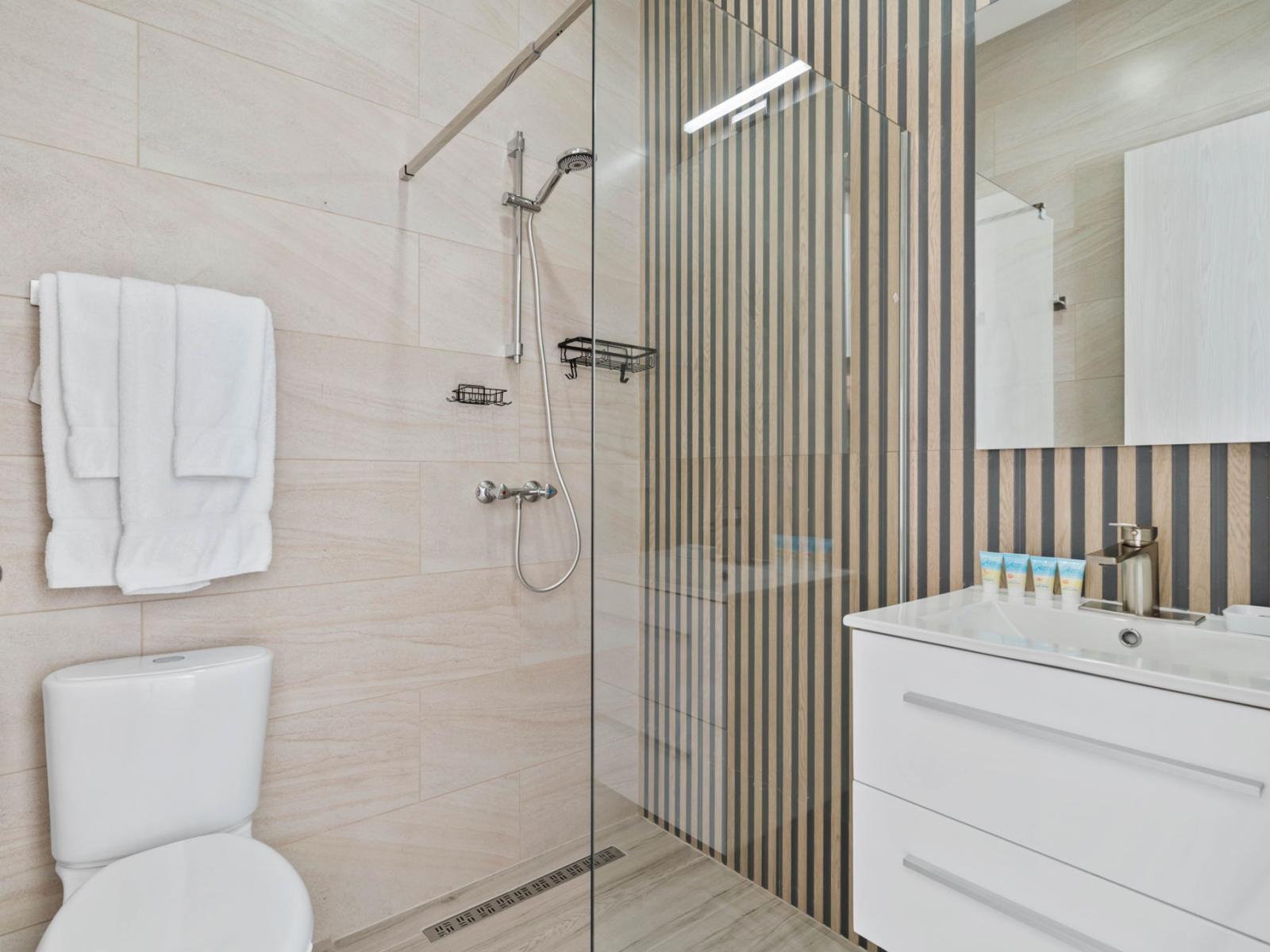 - Modern bathroom with a glass-enclosed shower and stylish striped accent wall - Sleek vanity with plenty of storage and bright lighting for a clean, organized look - Neutral tones and soft towels enhance the spa-like, relaxing atmosphere