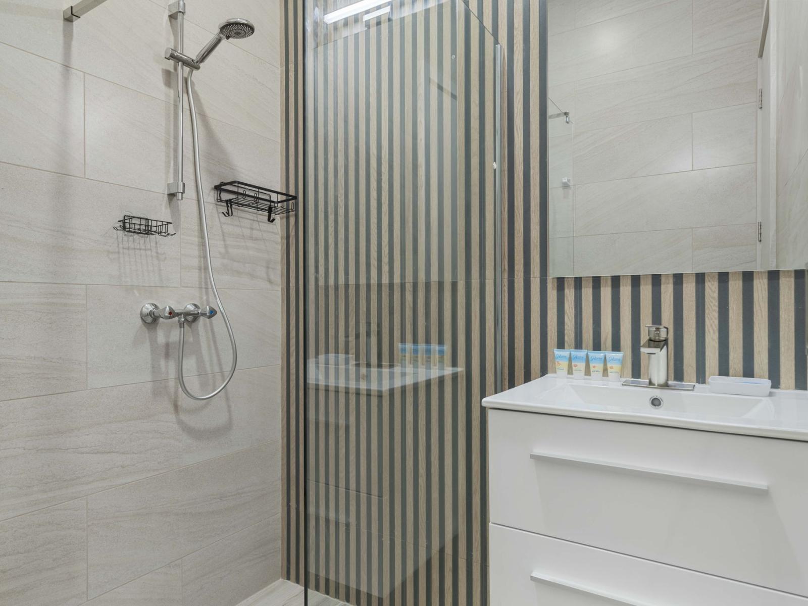 - Modern bathroom with a glass-enclosed shower and stylish striped accent wall - Sleek vanity with extra storage and clean lines for a minimalist look - Neutral tones and elegant tilework create a serene, spa-like atmosphere perfect for relaxation