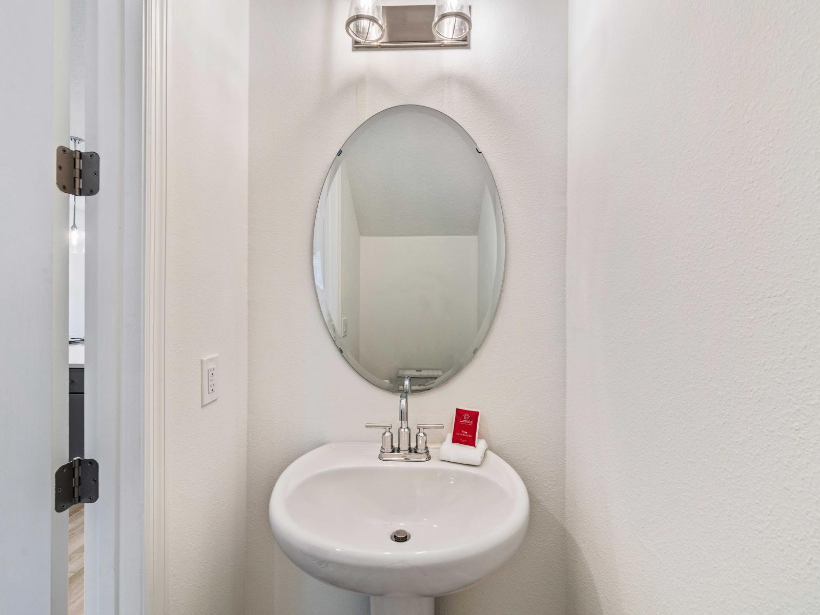 Stylish half bathroom features a sleek pedestal sink, maximizing space and functionality - Large oval mirror enhances the room's elegance, complemented by contemporary lighting fixtures - Conveniently located, offers quick and easy access