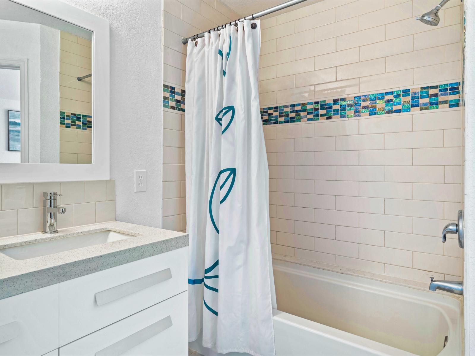 Modern bathroom featuring a bathtub and shower combo with stylish tile accents - Sleek vanity with plenty storage and a well-lit mirror for your grooming needs - Bright and clean design, providing a refreshing and comfortable space to relax