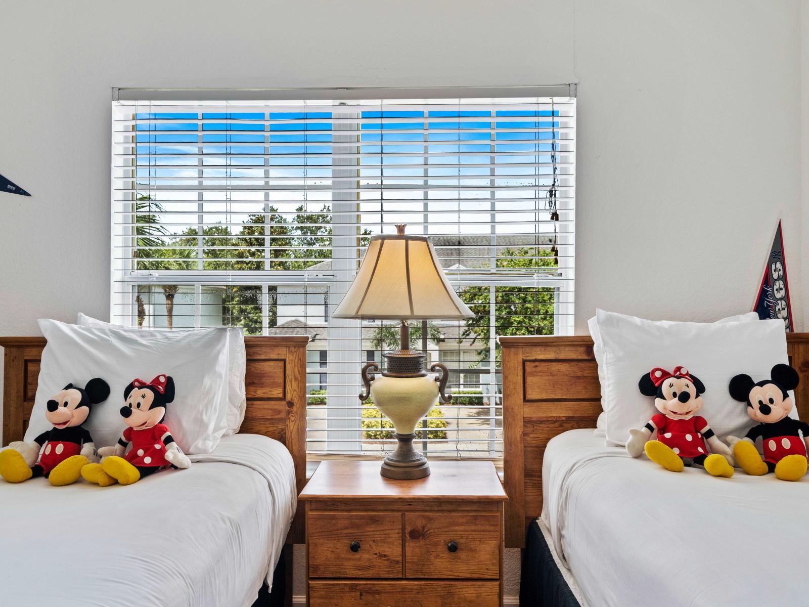 Cheerful bedroom with two single beds, each adorned with Mickey and Minnie Mouse plush toys - Window provides plenty of natural light, creating a bright and inviting space - Ideal for kids or guests, offering comfort and a touch of Disney magic