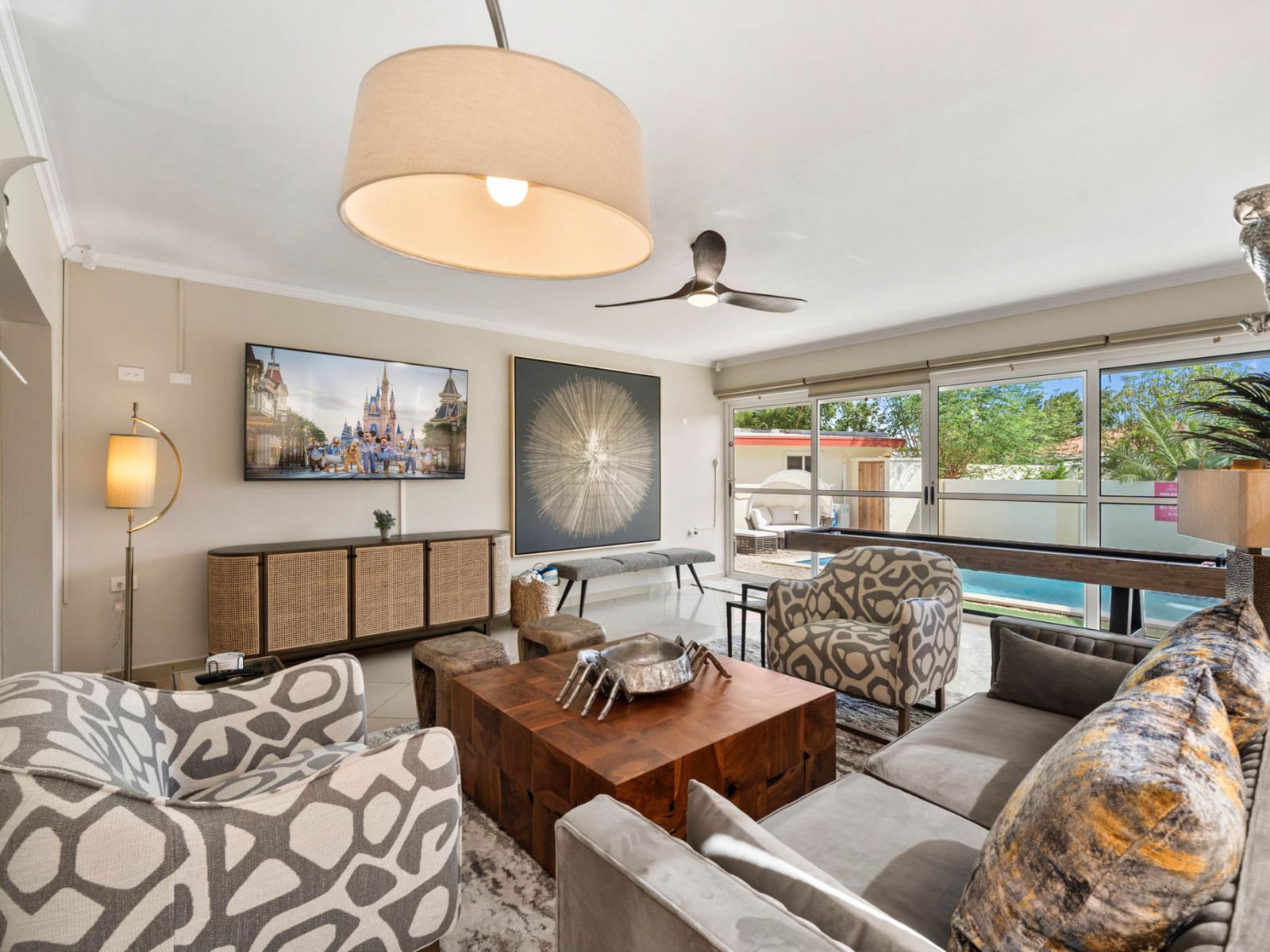 - Modern living room with patterned armchairs and a wooden coffee table - Glass doors fill the space with natural light, offering a clear view of the outdoor pool area - Stylish decor includes abstract art, a mounted TV, and elegant lighting fixtures