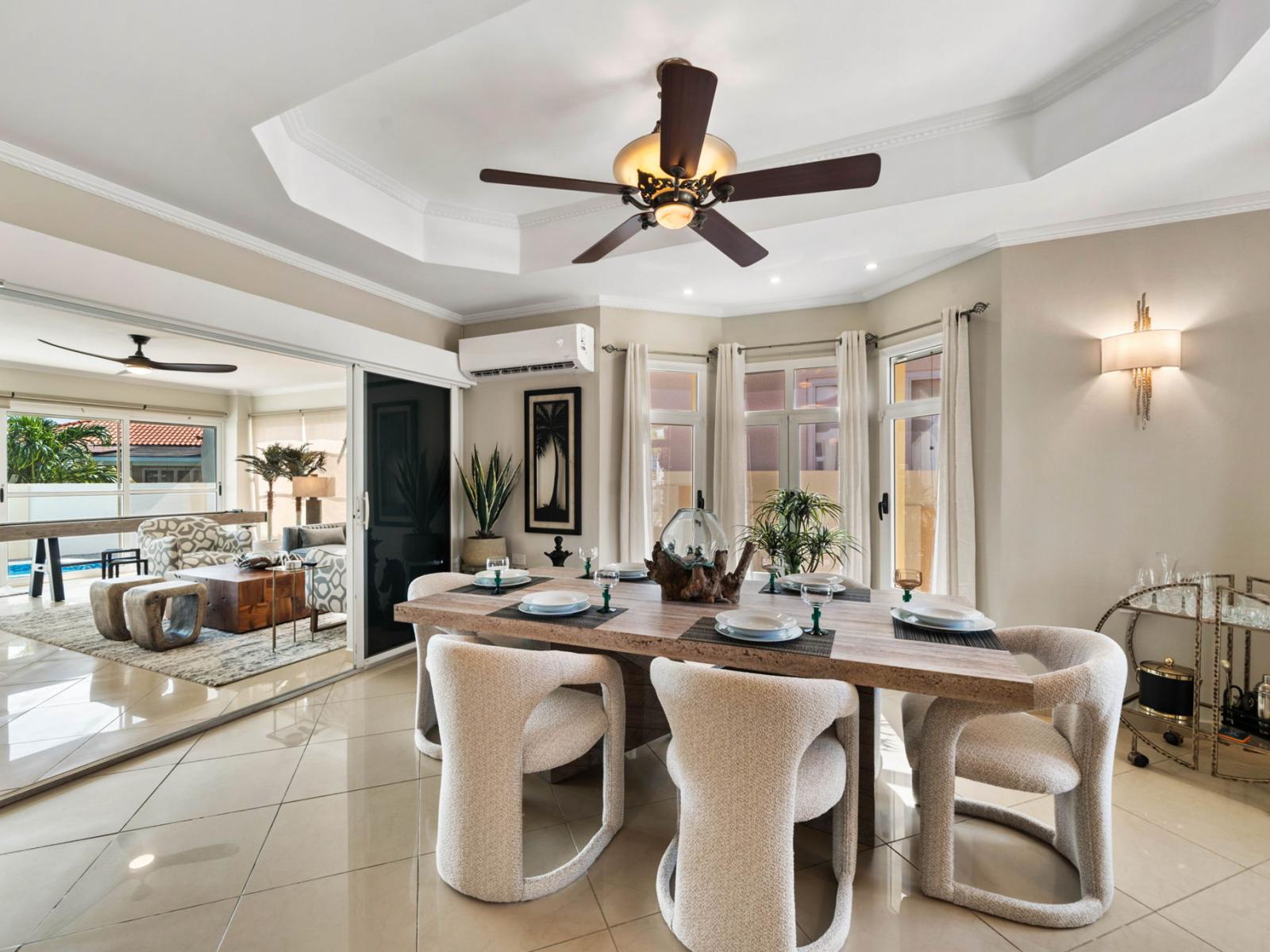 - Elegant dining area with a stylish wooden table set for a cozy gathering - Soft, cushioned chairs and ambient lighting create an inviting atmosphere - Open layout seamlessly connects to the living room and pool, perfect for entertaining