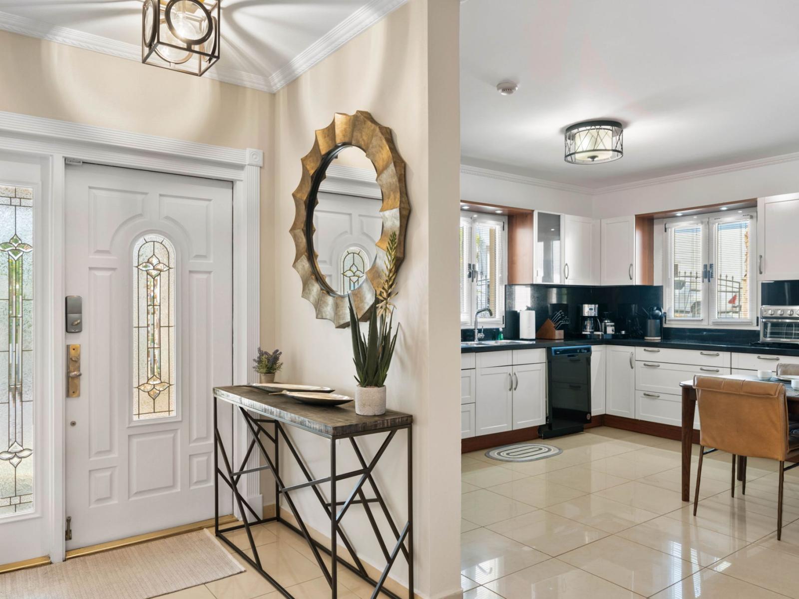 - Welcoming entryway with elegant details, including a decorative mirror and stylish console table - Natural light enhances the warmth of the space, leading into a modern kitchen - A perfect blend of sophistication and comfort greets you at the door