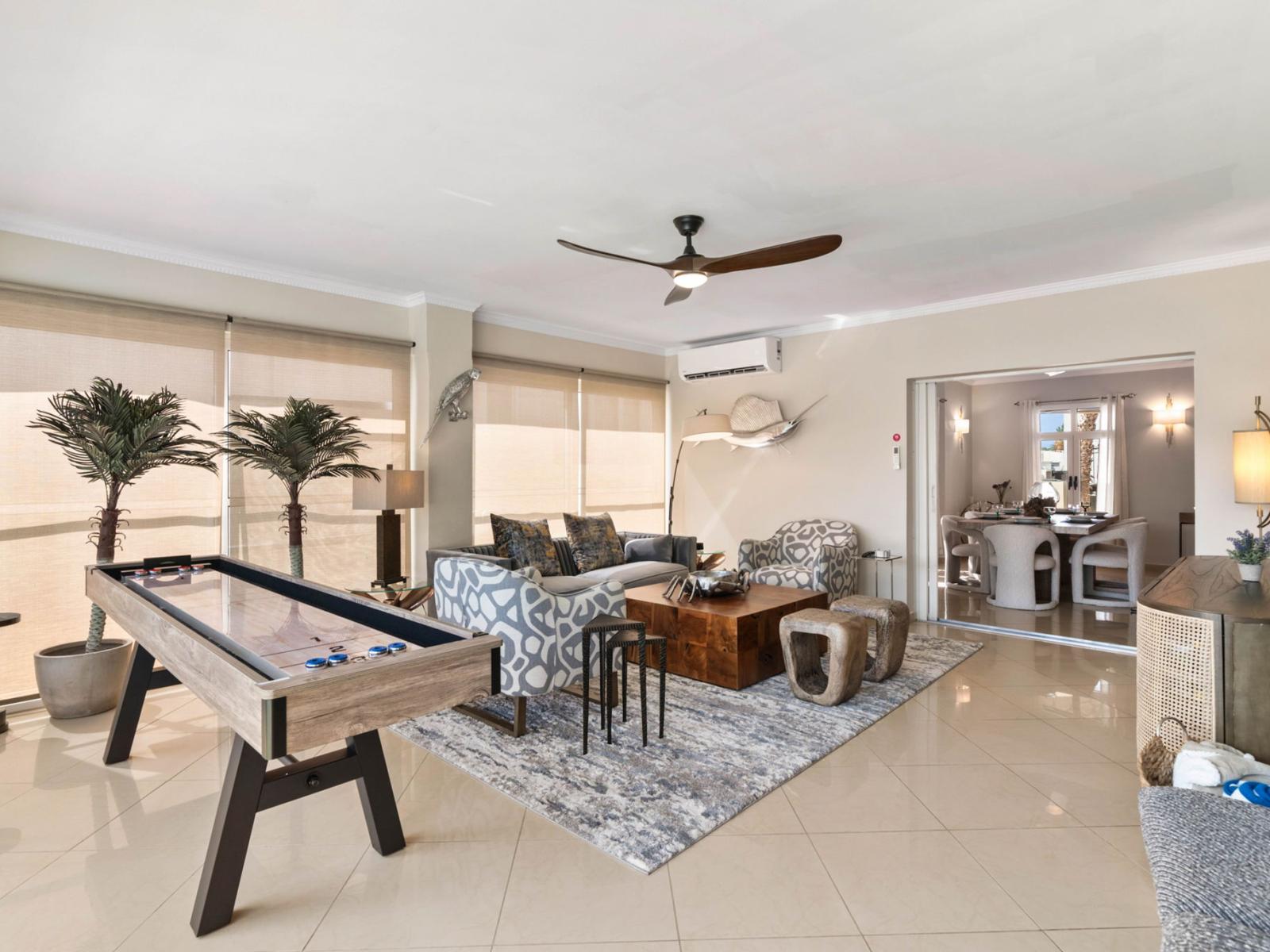 - Spacious living area featuring a shuffleboard table for entertainment and relaxation - Stylish seating arrangement with modern decor creates a welcoming atmosphere - Open layout provide plenty of natural light and seamless flow to the dining area