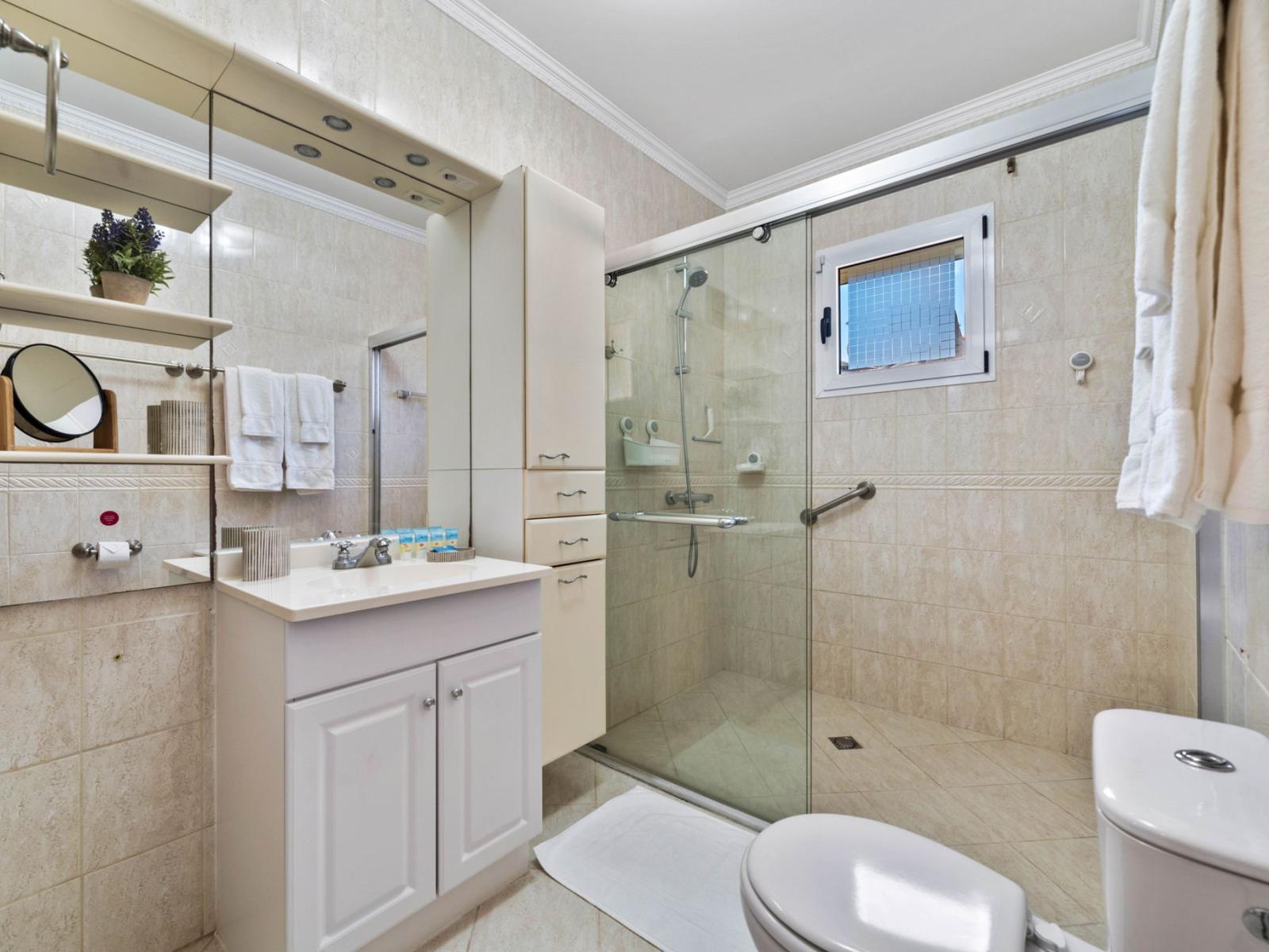 - Refreshing and modern bathroom with a sleek glass-enclosed shower, perfect for unwinding - Elegant white cabinetry and thoughtful storage combine style and practicality - Soft lighting and polished tiles create a serene, peaceful atmosphere