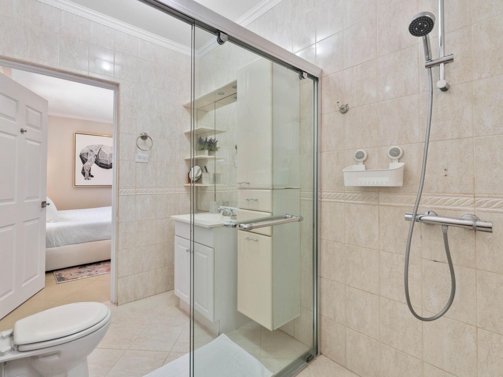 - Stylish bathroom featuring a sleek glass-enclosed shower and modern fixtures - Thoughtful design with plenty of storage and clean, neutral tones for a fresh look - Opens into a cozy bedroom, blending convenience with elegance in this tranquil space