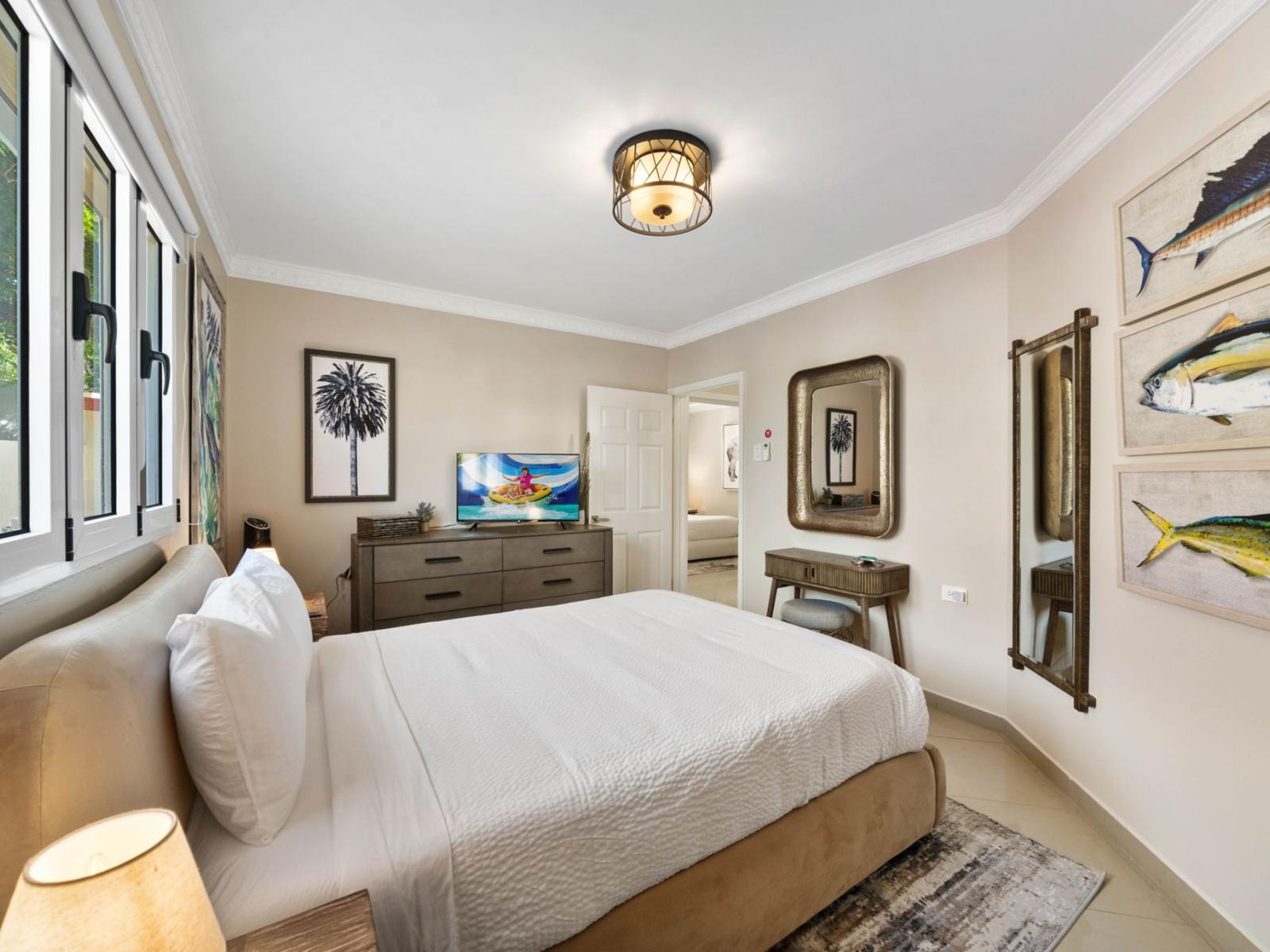 - Cozy bedroom with a plush queen-size bed and tasteful coastal-themed artwork - Natural light pours in through large windows, creating a bright and inviting space - Stylish mirror and modern dresser, adds elegance and comfort to this serene retreat