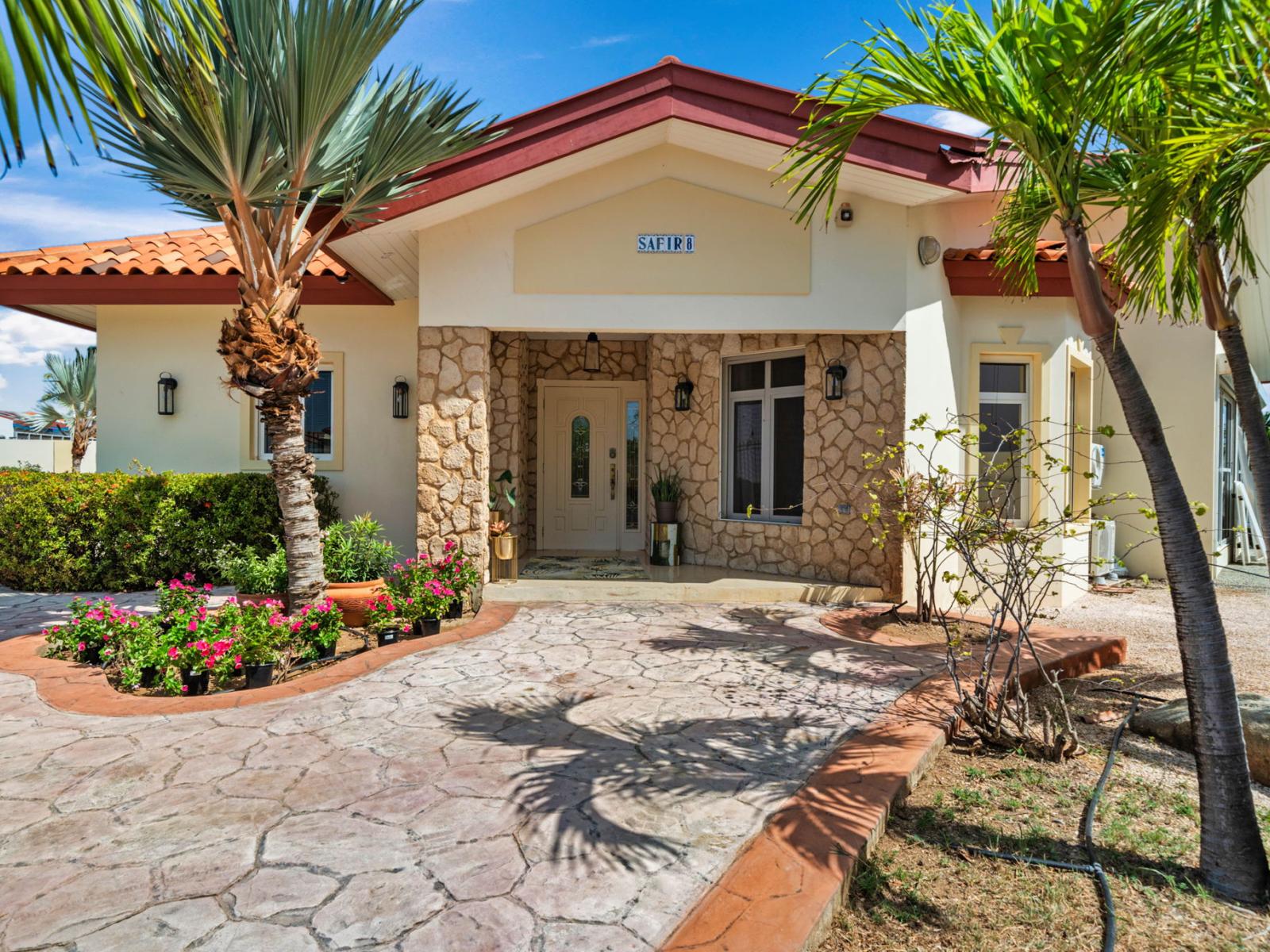 Charming stone-accented entrance surrounded by lush greenery and vibrant flowers.