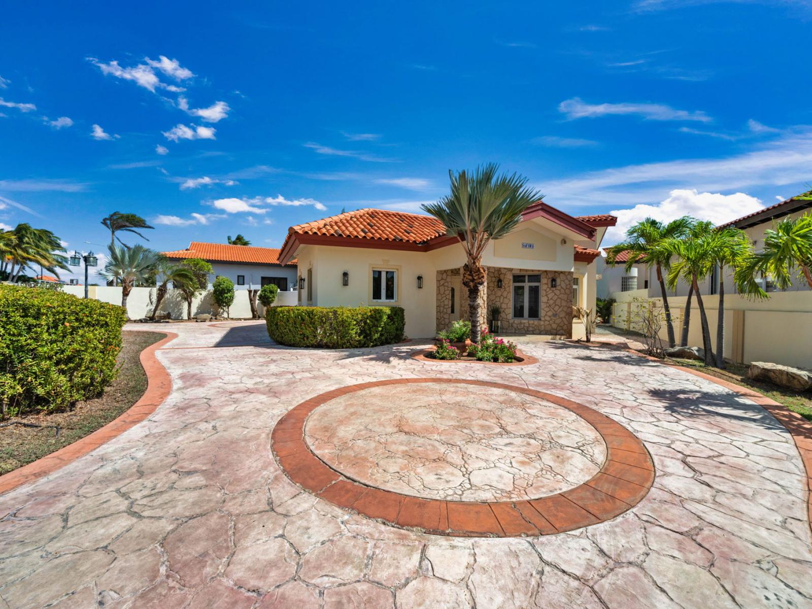 Expansive, beautifully designed driveway leading to a charming home with lush landscaping.