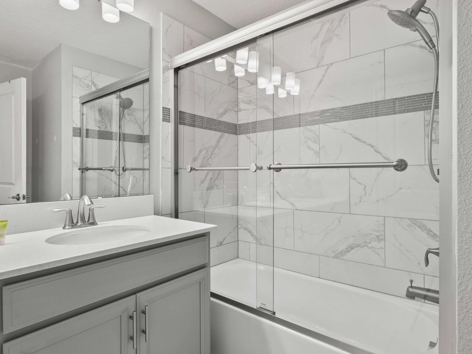 - A sleek design with a bathtub-shower combo, ideal for relaxation or a quick rinse - The modern marble-tiled walls and glass enclosure add a touch of calmness - Enjoy a refreshing and comfortable experience in this beautifully appointed space