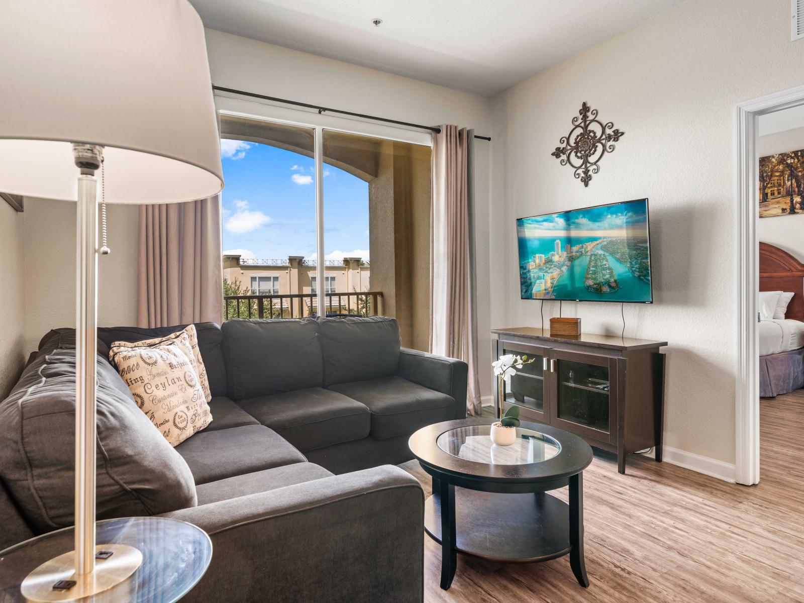 - Open living area with a plush sofa and sleek coffee table perfect for casual lounging - Features a smart TV and tasteful decor that enhances overall beauty of living space - Adjacent bedroom visible through an open doorway adding a connected feel