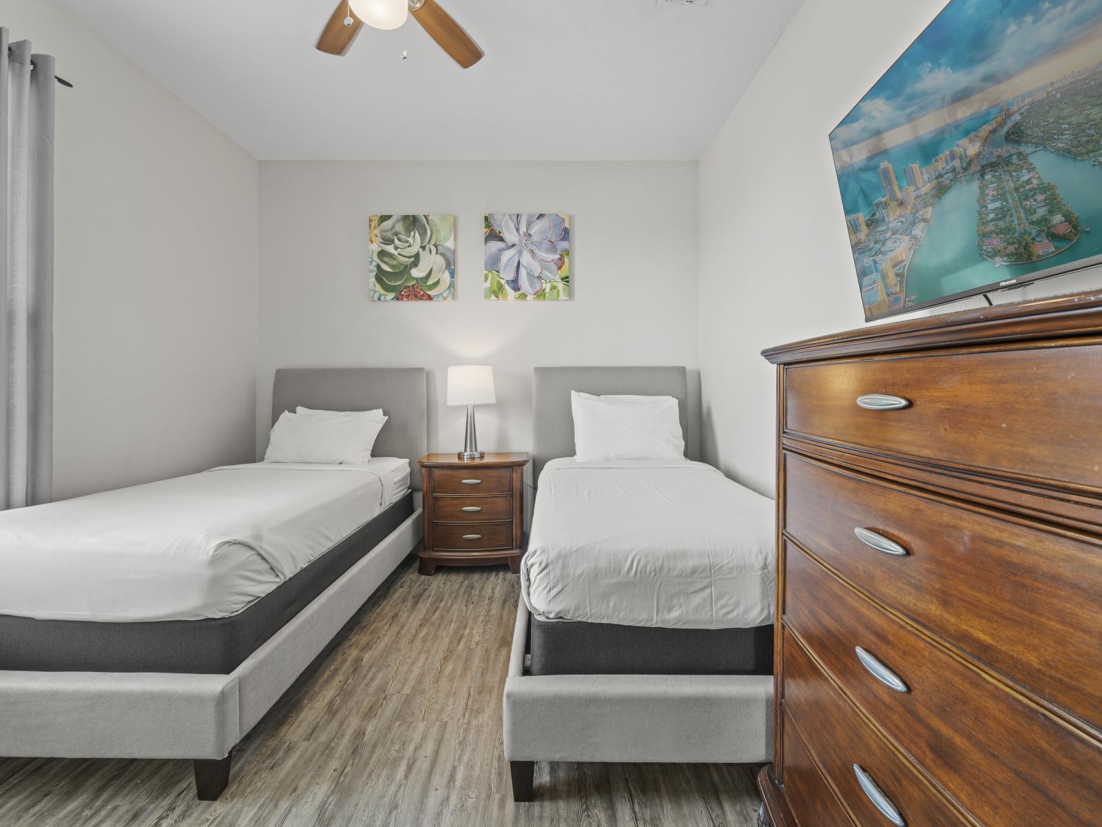 - Cozy bedroom with two single beds, perfect for accommodating guests or children - Room features a shared nightstand with a lamp, adding convenience and comfort - Large dresser and a smart TV provide generous storage and entertainment options