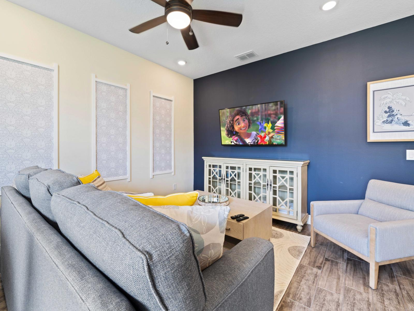 Vibrant living room with a plush gray sofa and matching armchair, perfect for relaxation - Navy accent wall highlights a mounted flat-screen TV, ideal for movie nights - Stylish cabinet, and elegant wall decor add a touch of charm and warmth