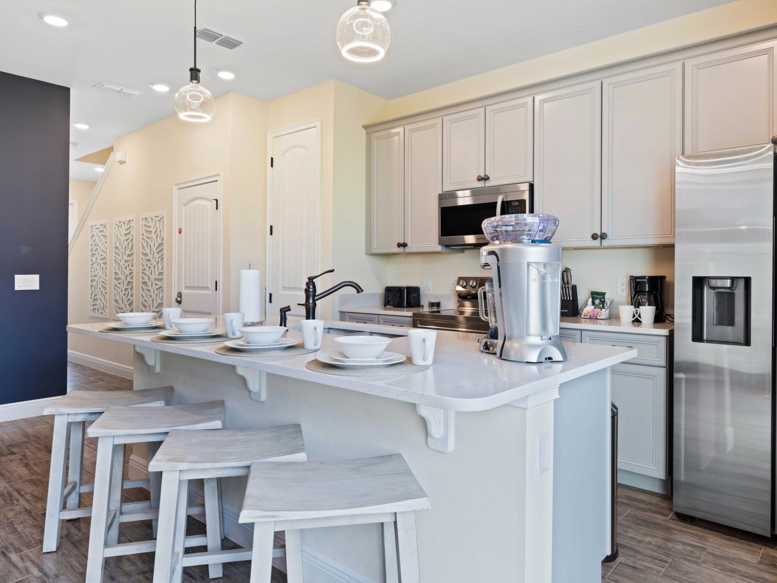 Sleek kitchen boasting stainless steel appliances and stylish light gray cabinets - Inviting breakfast bar with four stylish stools, perfectly set with white dishes and mugs - Eye-catching pendant lights complete the modern, elegant ambiance