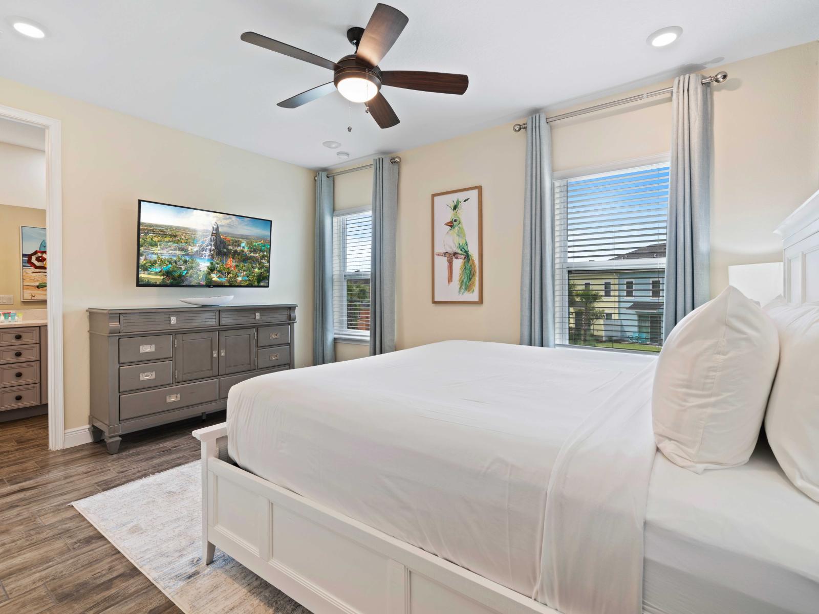 Spacious bedroom featuring a king-sized bed with crisp white bedding and fluffy pillows - Equipped with a private bathroom, a wall-mounted TV, and stylish gray furniture - Natural light from large windows enhances the bright, inviting atmosphere