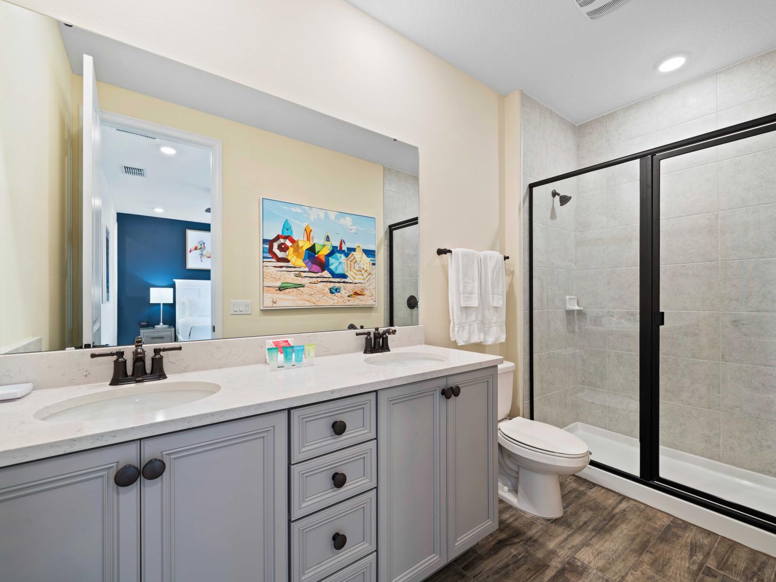 Modern bathroom with a walk-in shower featuring sleek black-framed glass doors - Double vanity with a white marble countertop, plenty of storage, and stylish faucets - Bright space, adorned with colorful wall art and neatly arranged towels