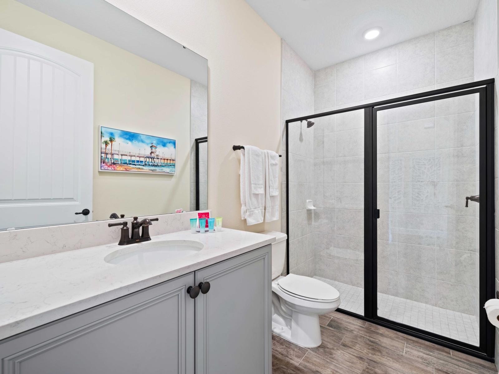 Modern bathroom with a spacious walk-in shower enclosed by black-framed glass doors - Elegant vanity with a white marble countertop, stylish faucet, and a large mirror - Bright and inviting atmosphere, enhanced by vibrant wall art