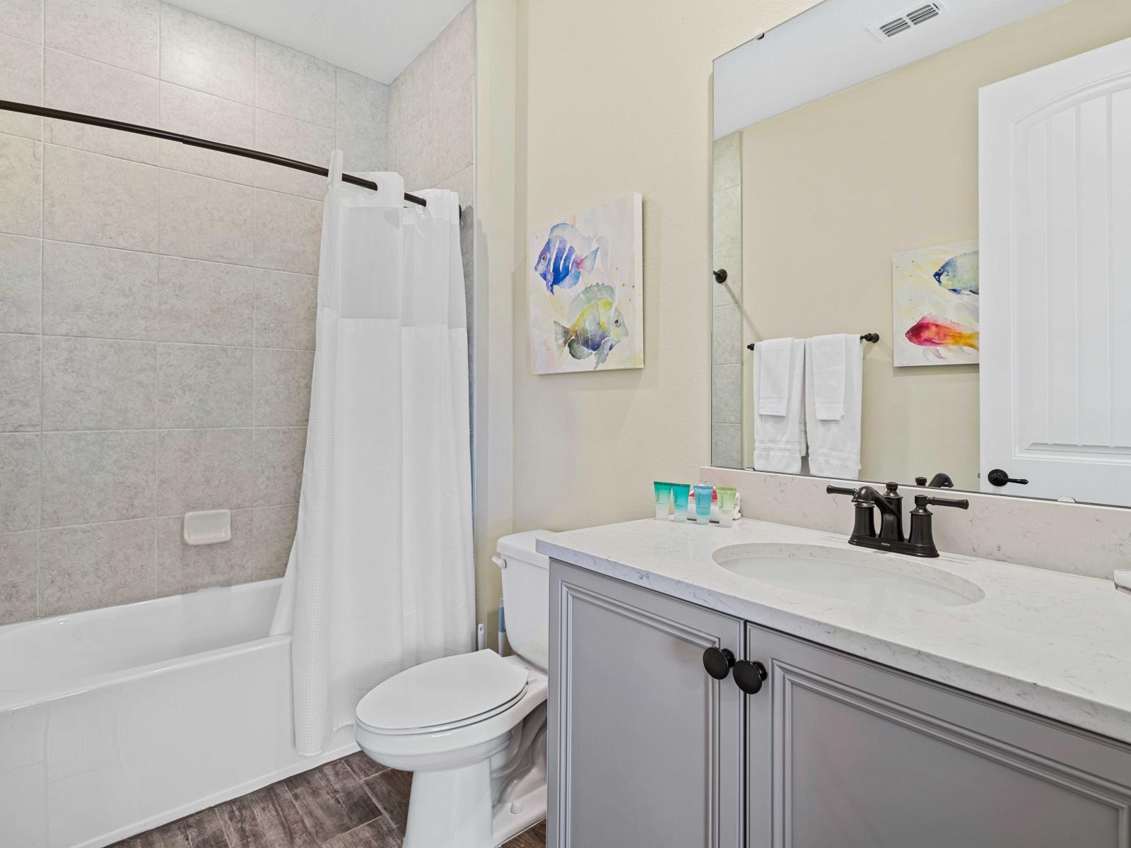 Bright bathroom featuring a combination bathtub and shower with a white curtain - Elegant vanity with a white marble countertop, black fixtures, and plenty of storage - Decorated with colorful fish-themed wall art and neatly arranged white towels