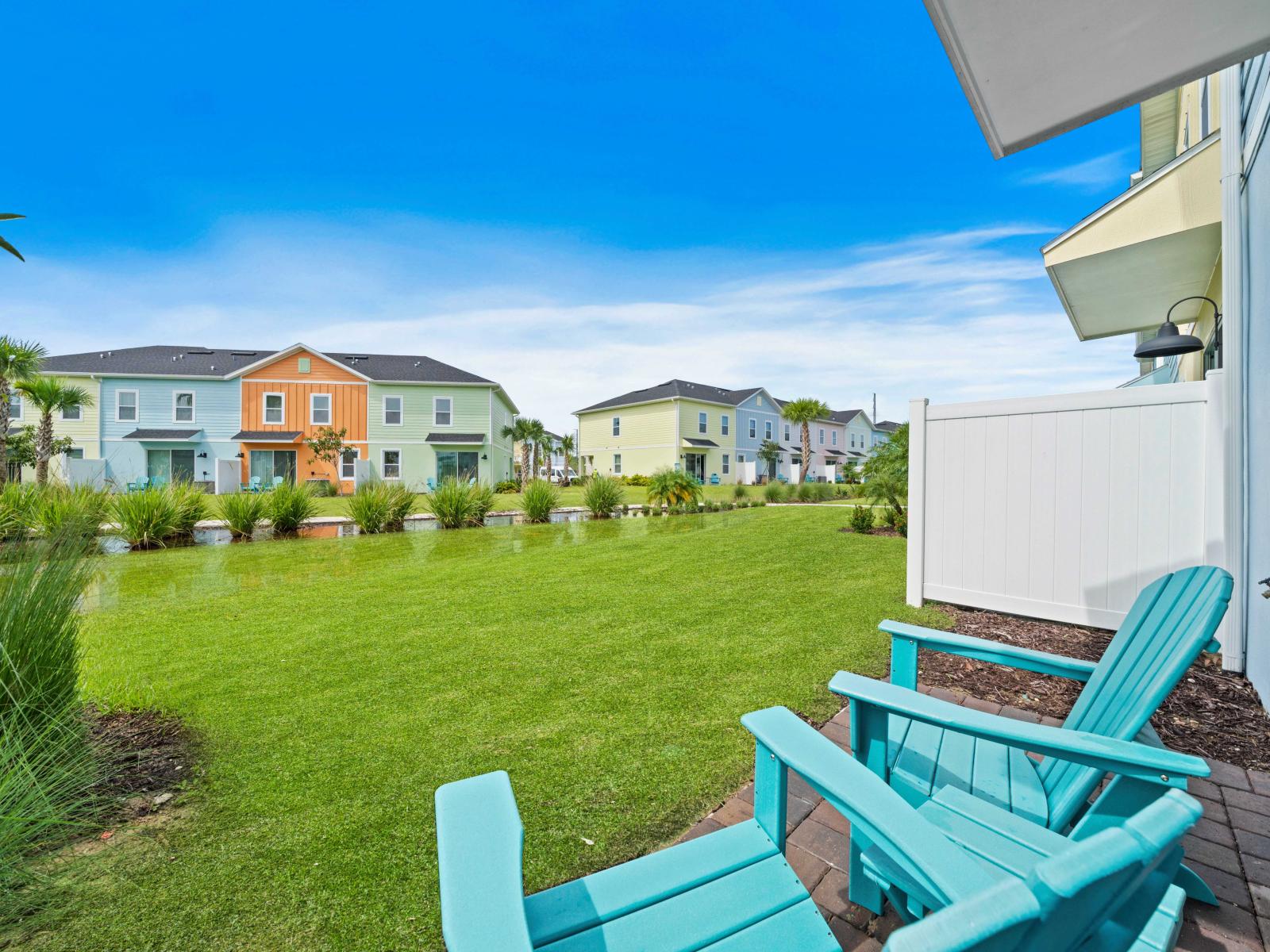 Relax in vibrant turquoise chairs and enjoy the serene view of colorful townhouses - The lush green patio and well-manicured landscaping create an inviting outdoor space - Perfect for a peaceful retreat or a friendly neighborhood gathering