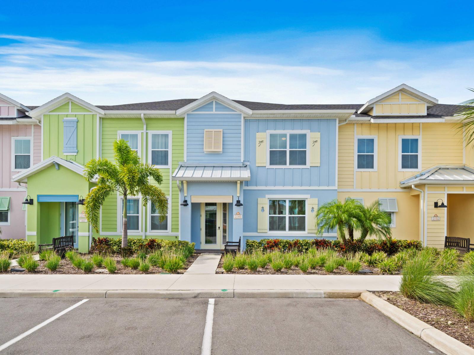 Vibrant townhouse entrance with pastel-colored exteriors, lush landscaping, and palm trees.