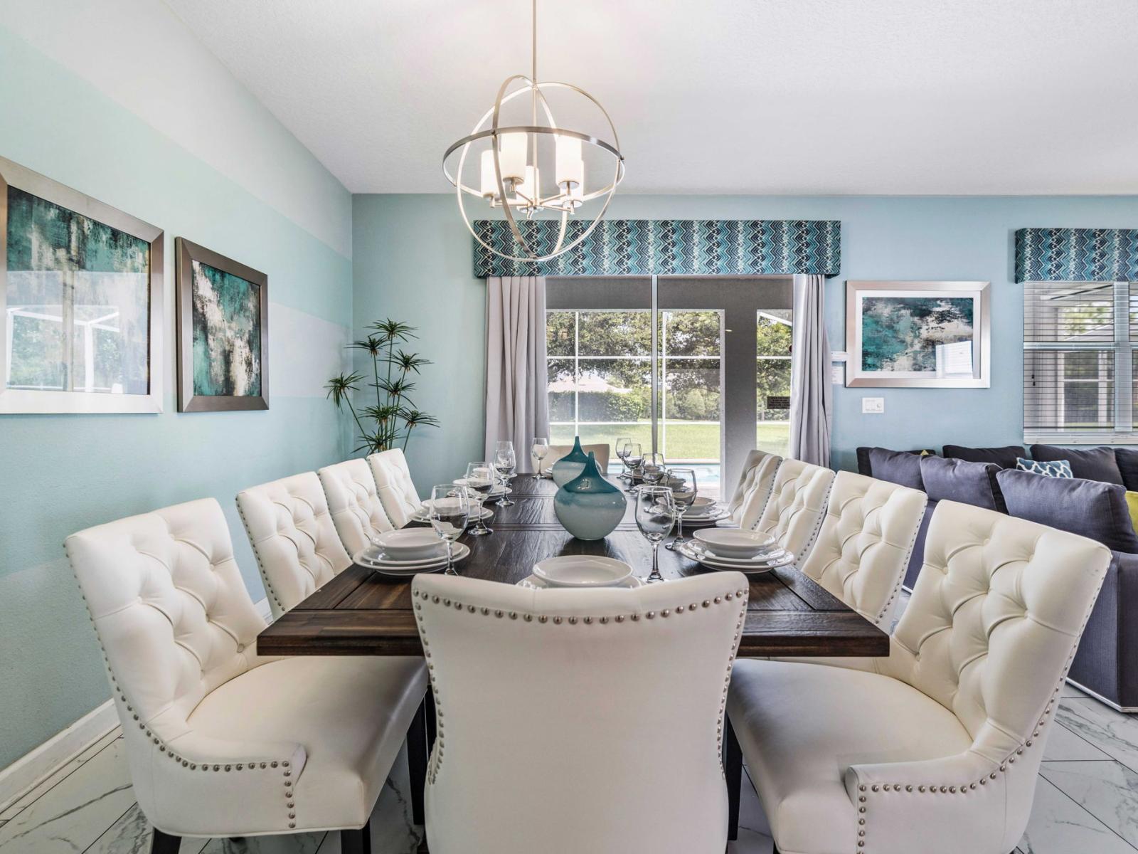 - Dining area is elegantly designed, featuring a large table surrounded by plush chairs - A stylish chandelier hangs above the table, providing a focal point - Artwork adorns the walls, while sliding glass doors lead to a well-lit backyard with pool