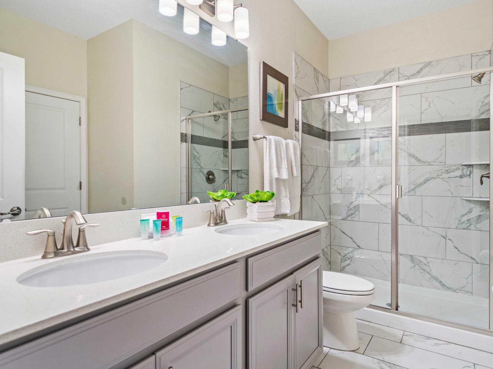 - Bathroom featuring a sleek double sink vanity with plenty of counter space - A large, glass-enclosed shower stands out with its modern tile design - The neutral tones of the bathroom are complemented by the inclusion of decorative plants