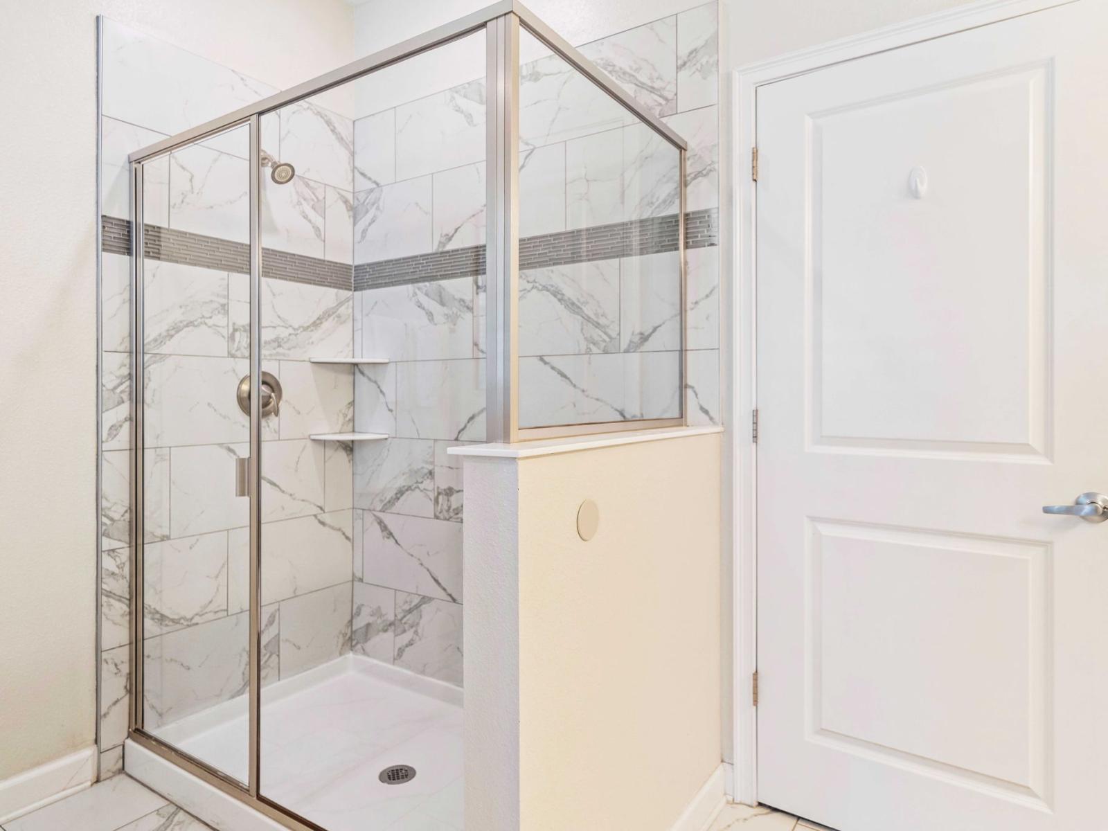 - Shower features sleek glass doors and intricate tile work, contributing to overall aesthetic appeal - Neutral color scheme that enhances the room's airy feel - Convenient shelving within the shower provides space for storing toiletries