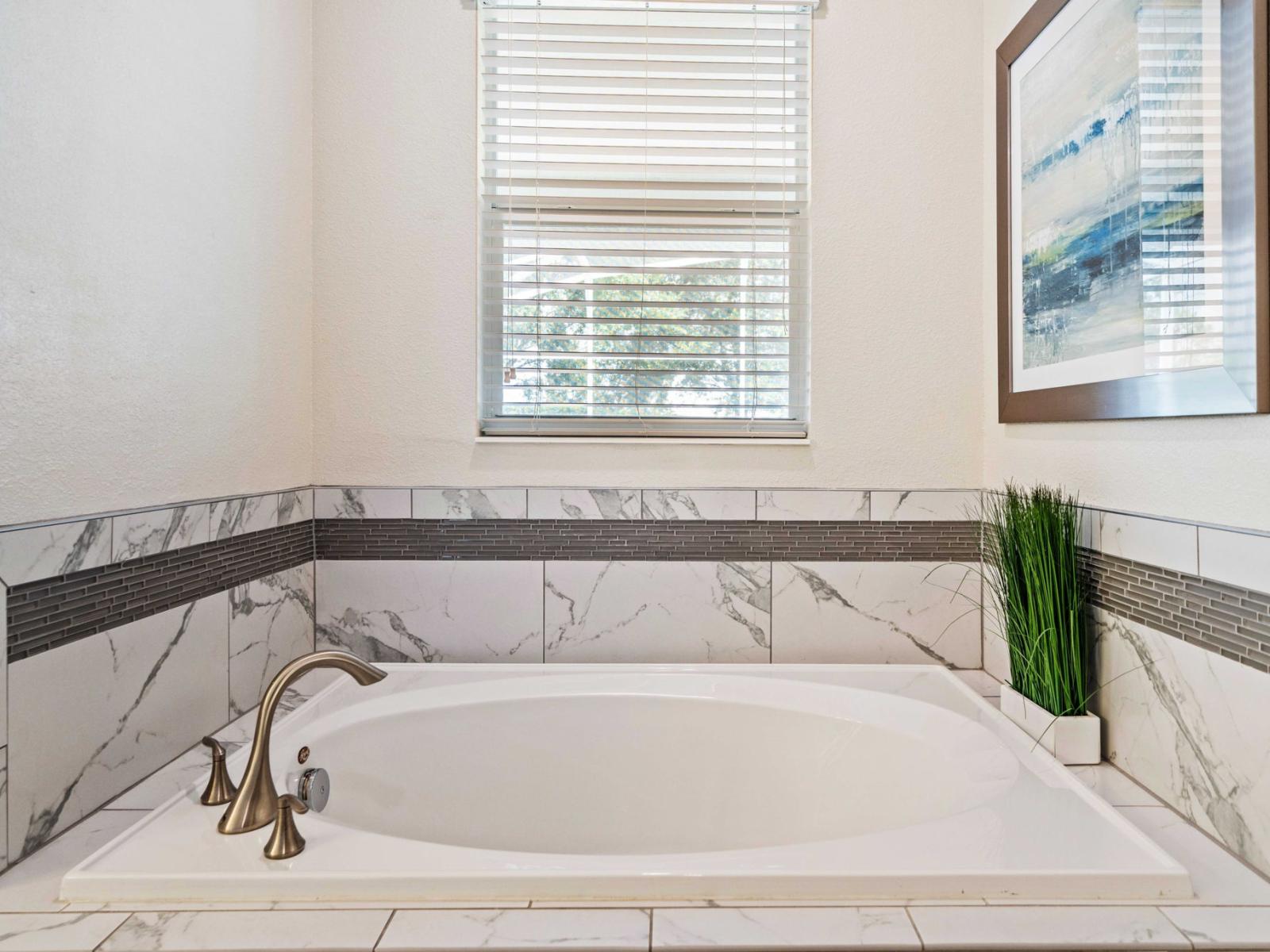 - Deep soaking tub surrounded by elegant marble tile accents, creating a serene atmosphere for relaxation - High-quality fixtures, including stylish faucets enhance the room's upscale feel - A perfect spot to unwind after a long day of exploration