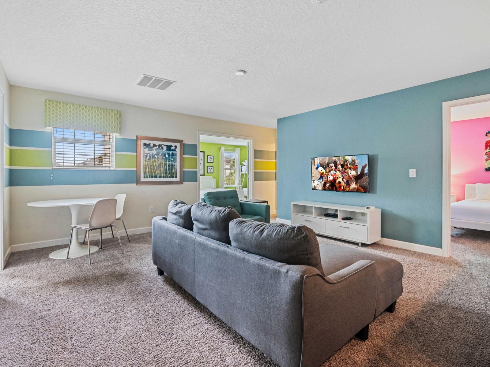 - Loft area is designed for comfort and entertainment, featuring a cozy sectional sofa and smart TV - Vibrant wall colors and modern decor elements create a inviting atmosphere - An adjacent small dining table serves as perfect spot for casual meals