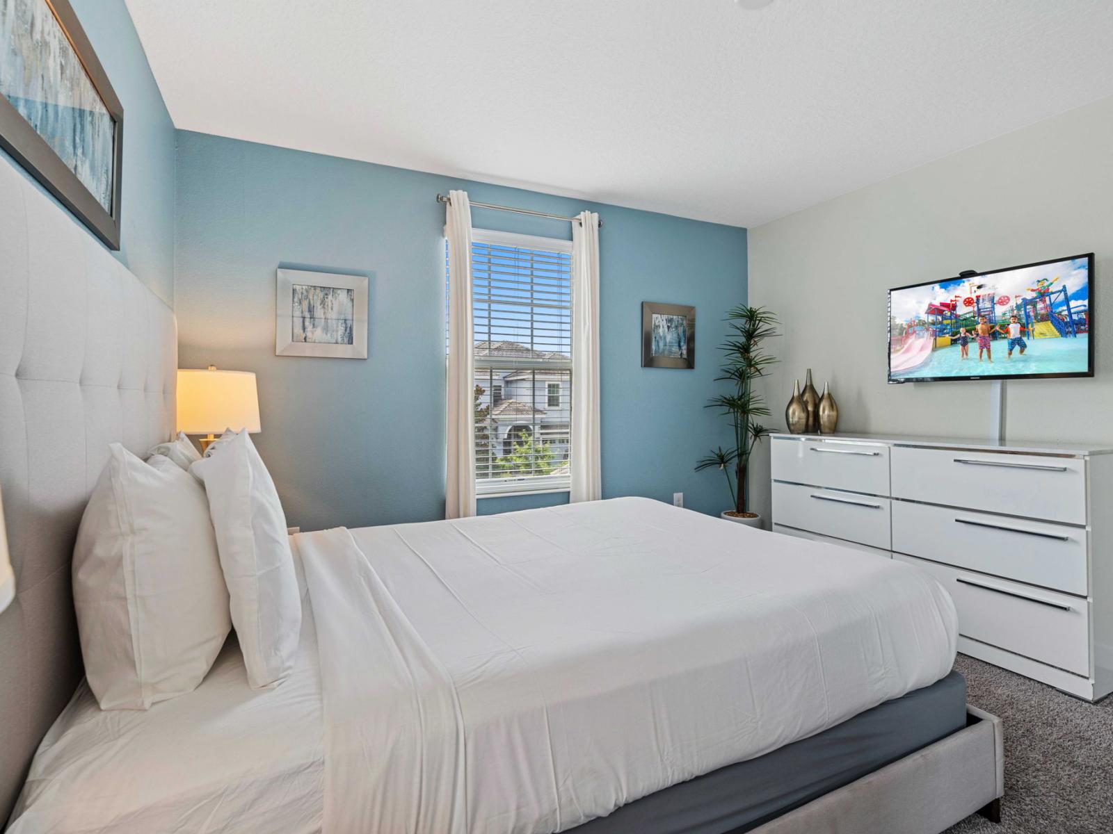 - Bedroom features a queen-sized bed that promotes relaxation and comfort - The soft blue accent wall and white furniture create a calming environment - Additional elements include a flat-screen TV, and thoughtfully chosen decor pieces