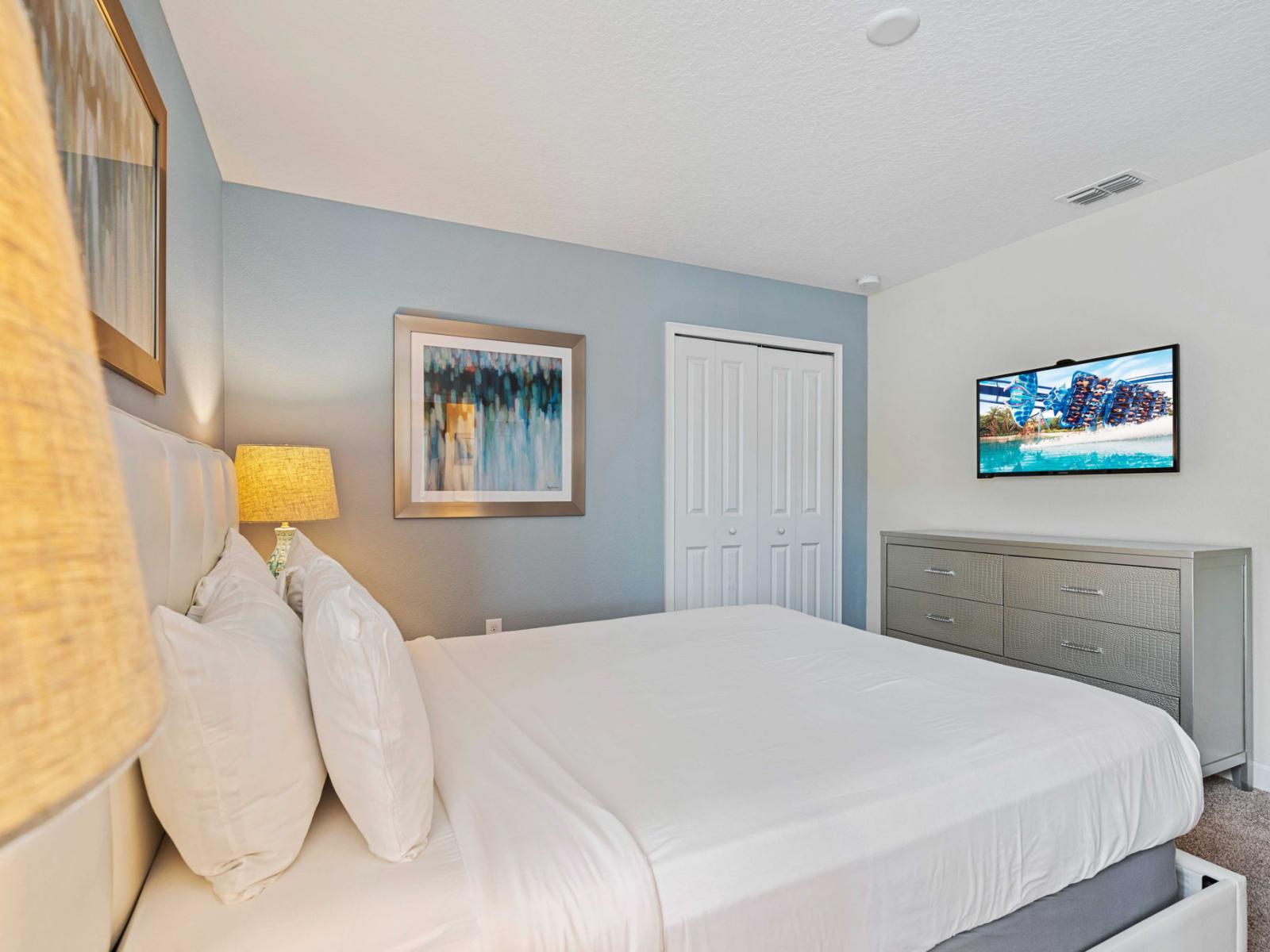 - Spacious bedroom with a comfortable queen sized bed, smart TV and light blue walls - Modern artwork and a bedside lamp adding warmth to the space - Combines functionality and style, ensuring the room is both practical and aesthetically pleasing