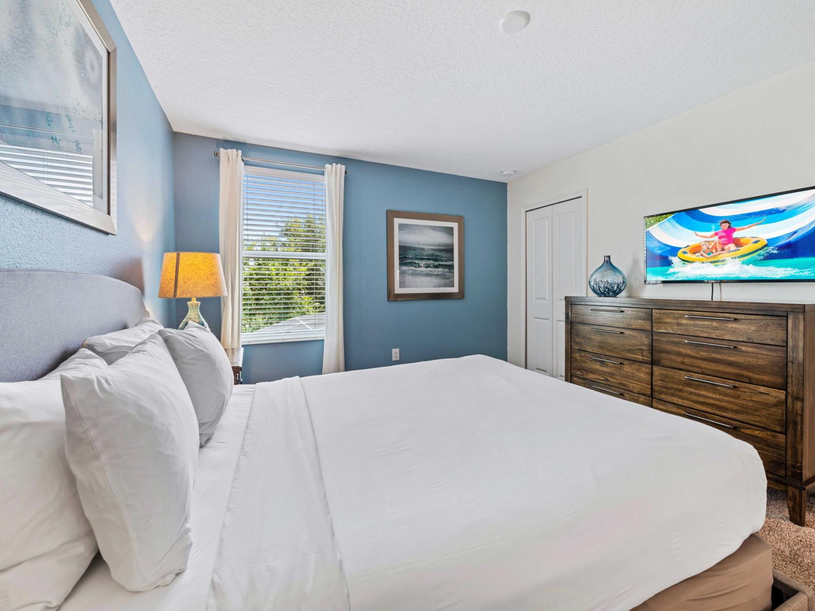 - Bedroom features a queen set against soft blue walls that exude tranquility - Smart TV provides entertainment, making the room both functional and relaxing - The window offers a view of the outdoors, allowing natural light to brighten the space