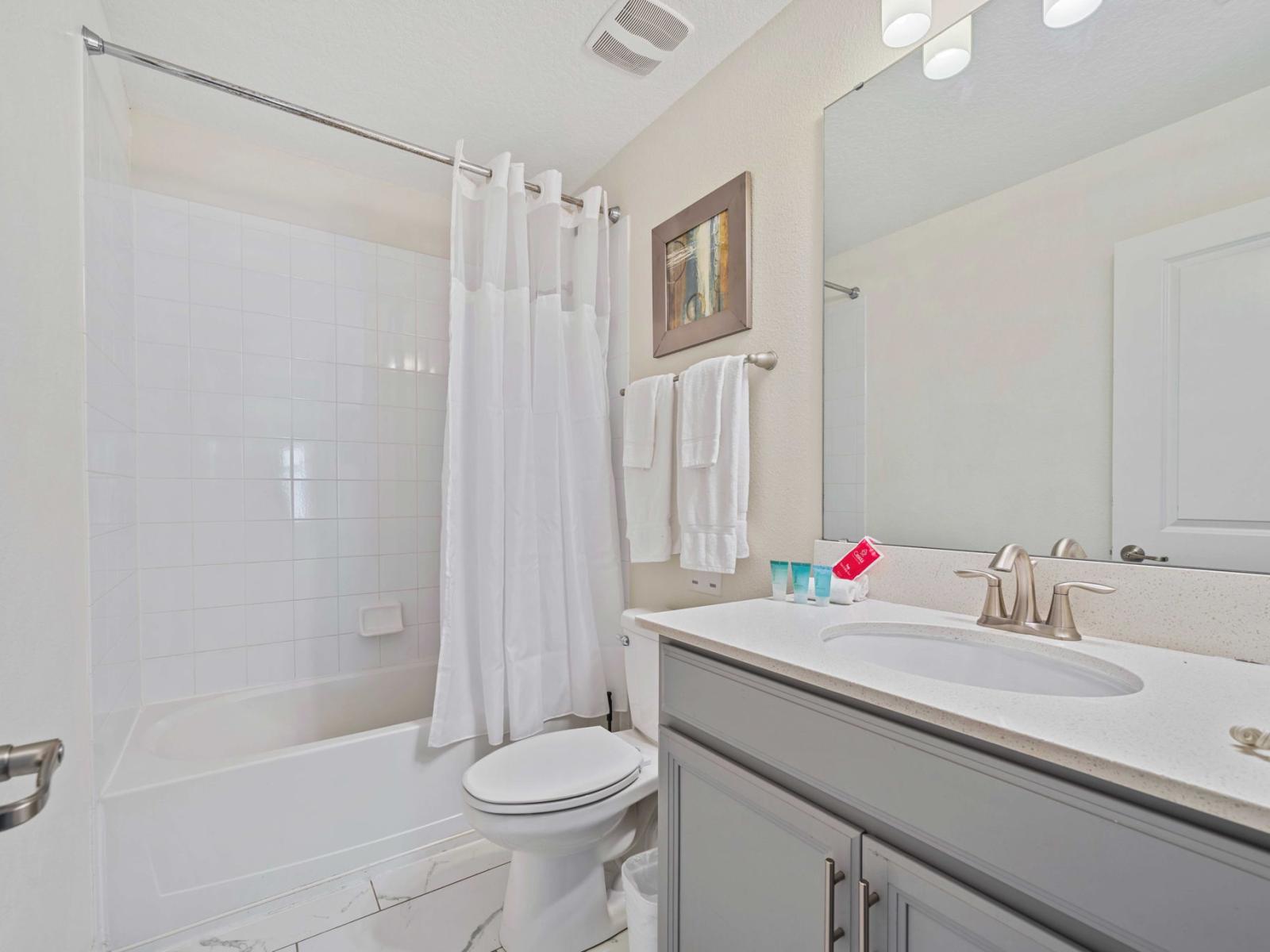 - Bathroom boasts a combination bathtub and shower, enclosed a curtain for privacy and functionality - The vanity featuring a wide mirror and tasteful decor that includes framed artwork and accessories - Cabinetry adds a modern touch to the space