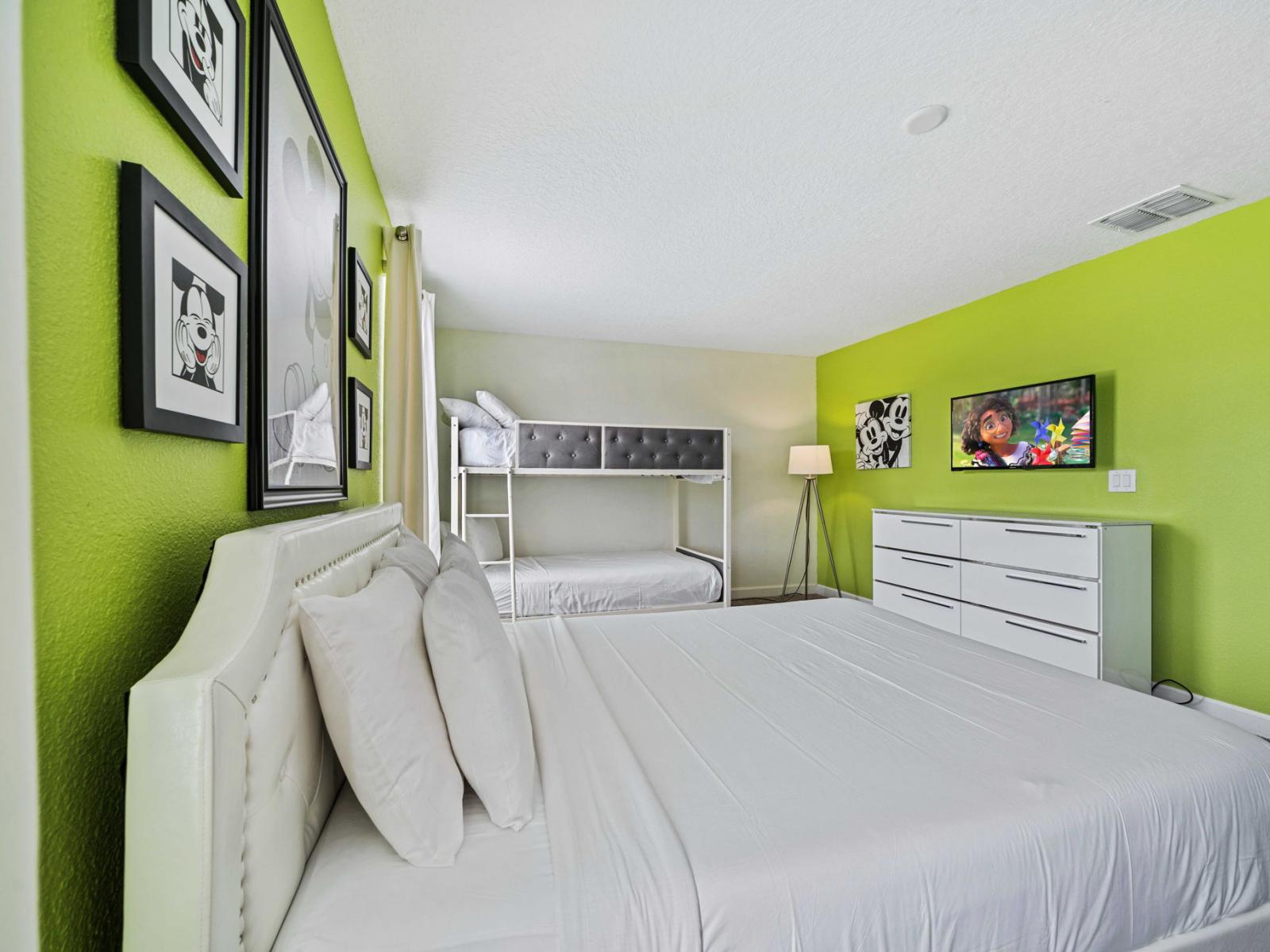 - This bedroom is featuring a double bed alongside bunk beds, perfect for families or groups - The vibrant green accent wall adds a playful touch , complemented by Mickey Mouse themed decor - Modern furnishings complete the room's functional design