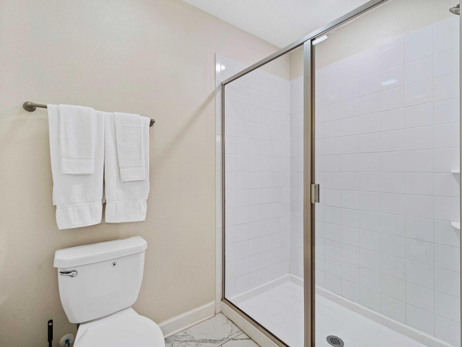 - Bathroom with spacious walk-in shower, enclosed by glass doors that give a contemporary look - White toilet is paired with matching towels, providing a cohesive and fresh aesthetic - Decor is kept simple with functional layout, ensuring convenience