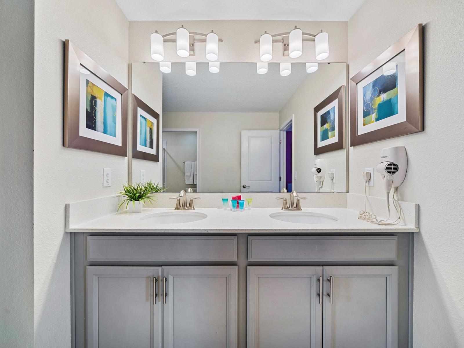 - Double sink vanity with sleek white countertop and modern fixtures - Large mirror with bright, contemporary light fixtures above - Simple, modern decor with framed abstract art and a small potted plant