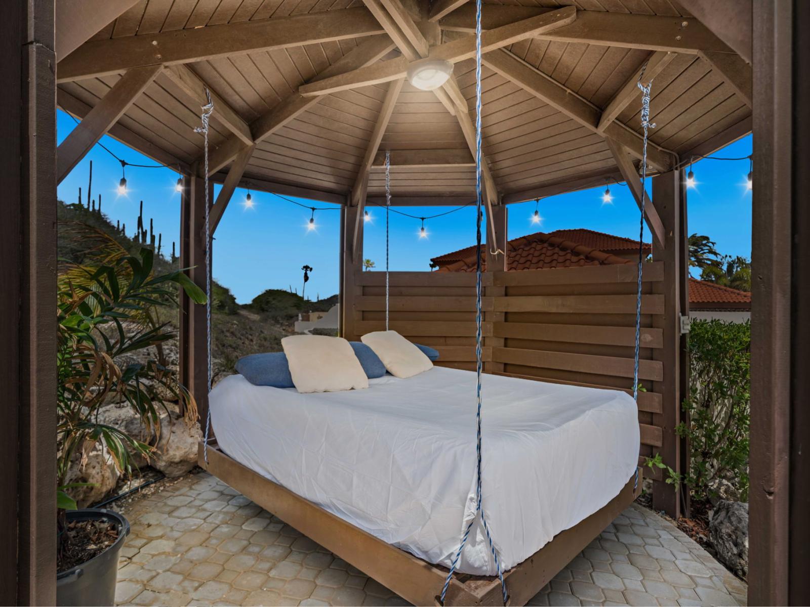 Enjoy a relaxing evening in this cozy outdoor lounge area with a comfortable bed swing - The backdrop of a beautiful sunset enhances the ambiance, making it an ideal place to unwind - Surrounded by natural scenery, this spot offers a serene retreat