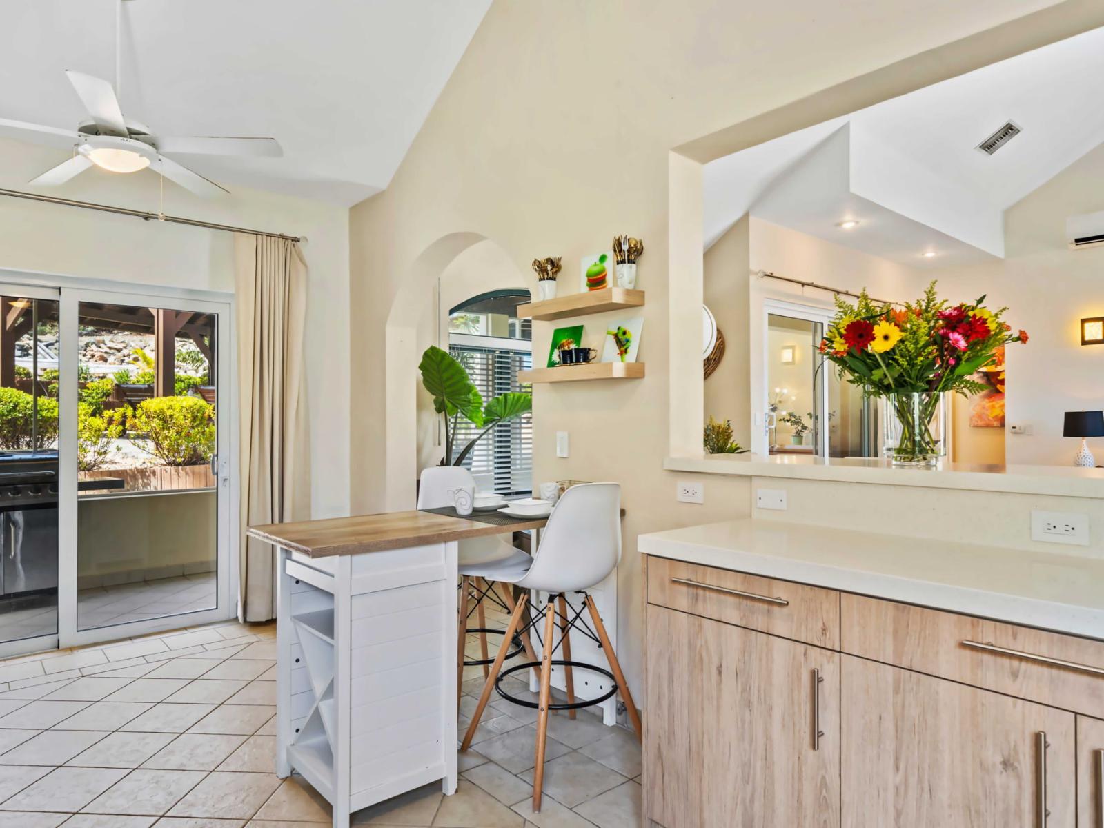 The kitchen features a cozy breakfast bar with stylish white stools for casual dining - Glass doors open to an outdoor area with a barbecue grill, perfect for entertaining - Bright flowers and open shelves add a touch of charm to the place