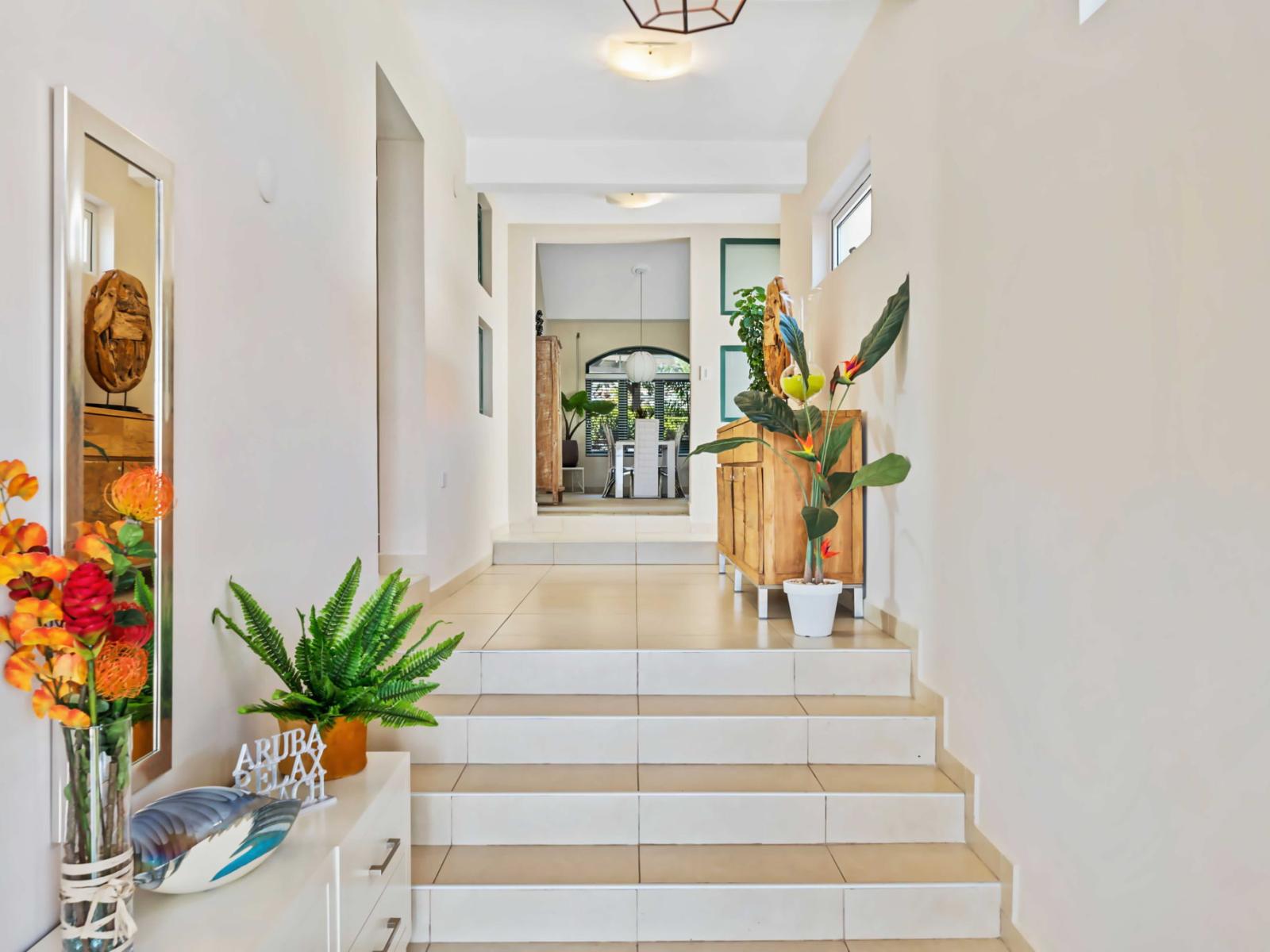 A bright hallway leads to the bedrooms, adorned with vibrant plants and decor - Steps add depth to the hallway, which features a blend of modern and rustic furnishings - Large windows and strategic lighting keep the space airy and inviting