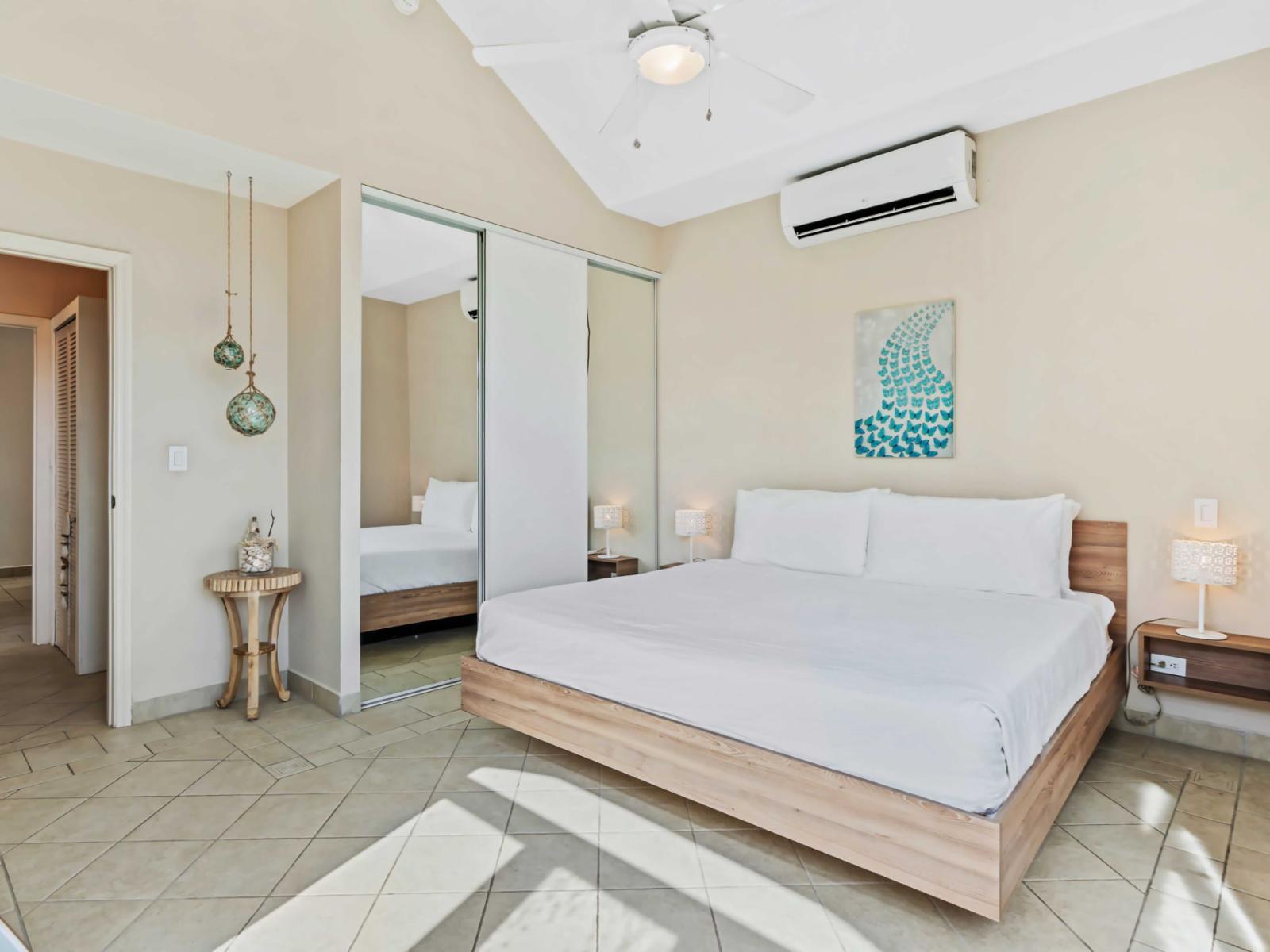 Bedroom features an air conditioner and attached bathroom for added convenience - The room is decorated with soft, neutral tones and accented with hanging pendant lights - A mirrored closet door enhances the sense of space and light in the room