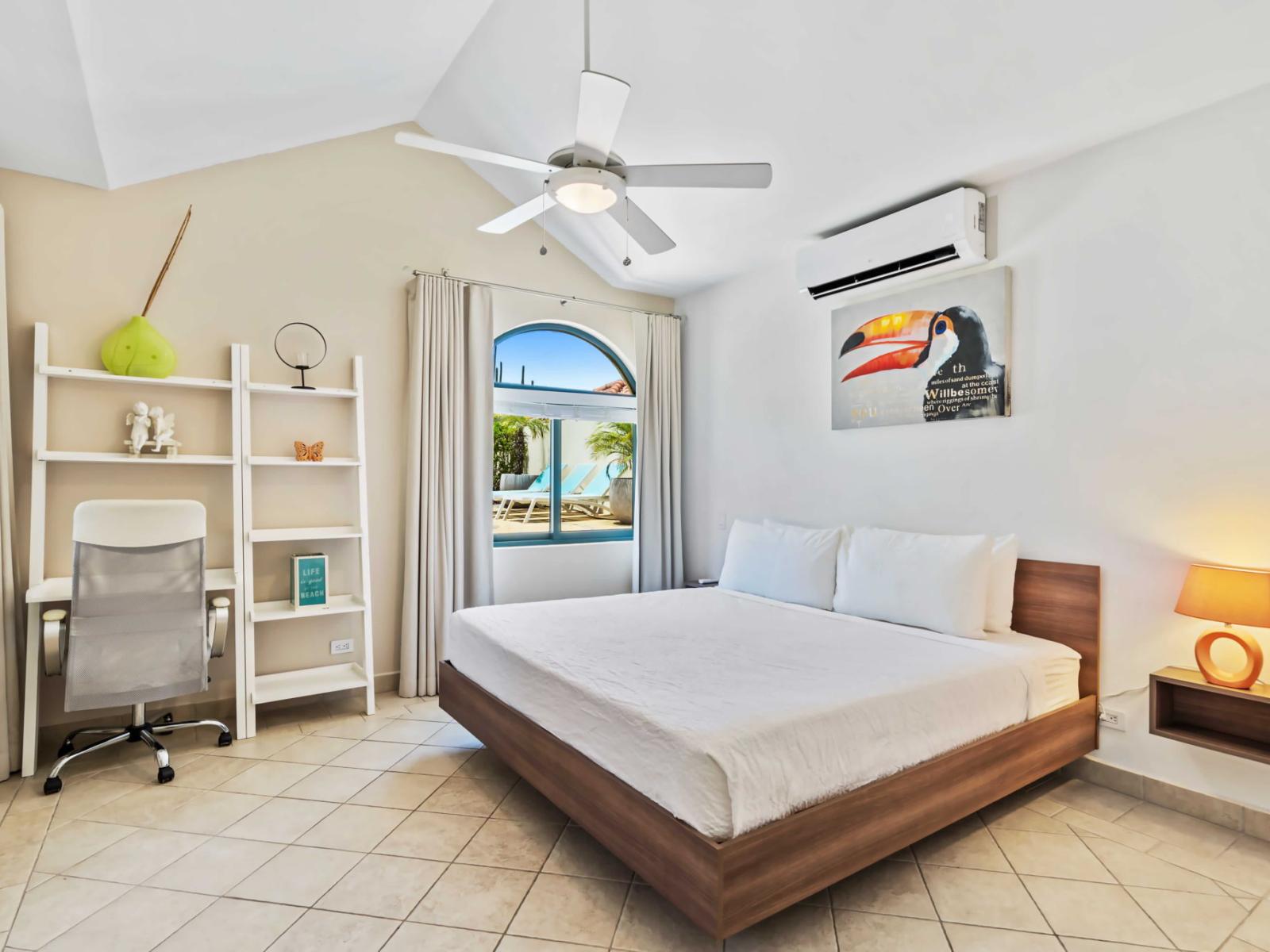 Bedroom features a comfortable king-size bed with a modern wooden frame - Window with an arched top provides a view of the pool area, allowing natural light to fill the room - The room includes a white desk and chair, perfect for a workspace