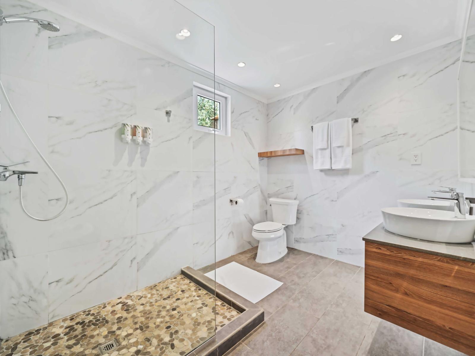 Beautiful marble-patterned tiles bathroom, creating a cohesive and elegant look - The bathroom includes a modern toilet and an open wooden shelf for additional storage - Recessed lighting and a small window ensure the space is well-lit