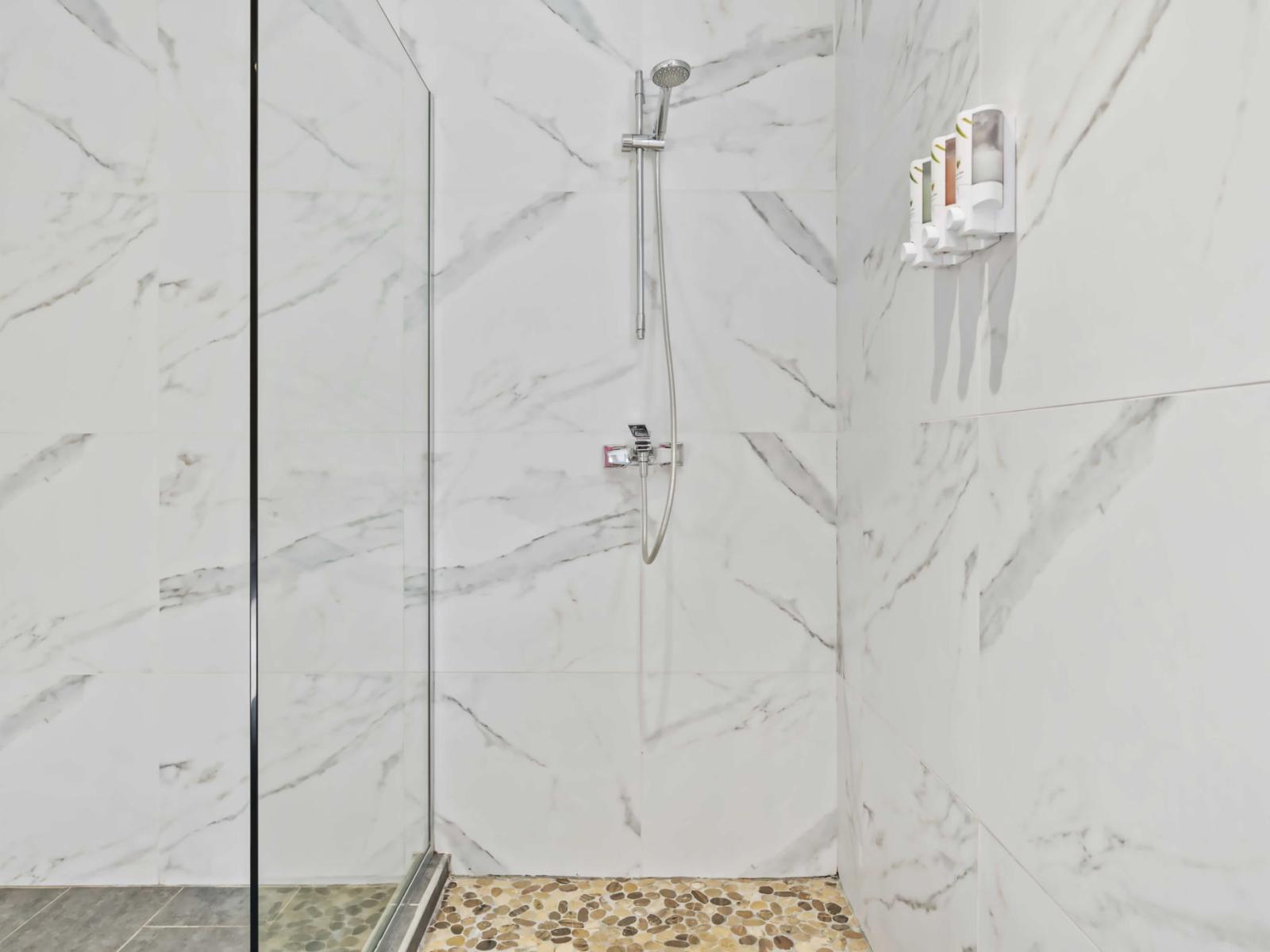 Convenient wall-mounted dispensers for toiletries are included within the shower area - The minimalist design and high-quality finishes contribute to a serene and spa-like atmosphere - Floor is adorned with pebble tiles, adding a stylish element