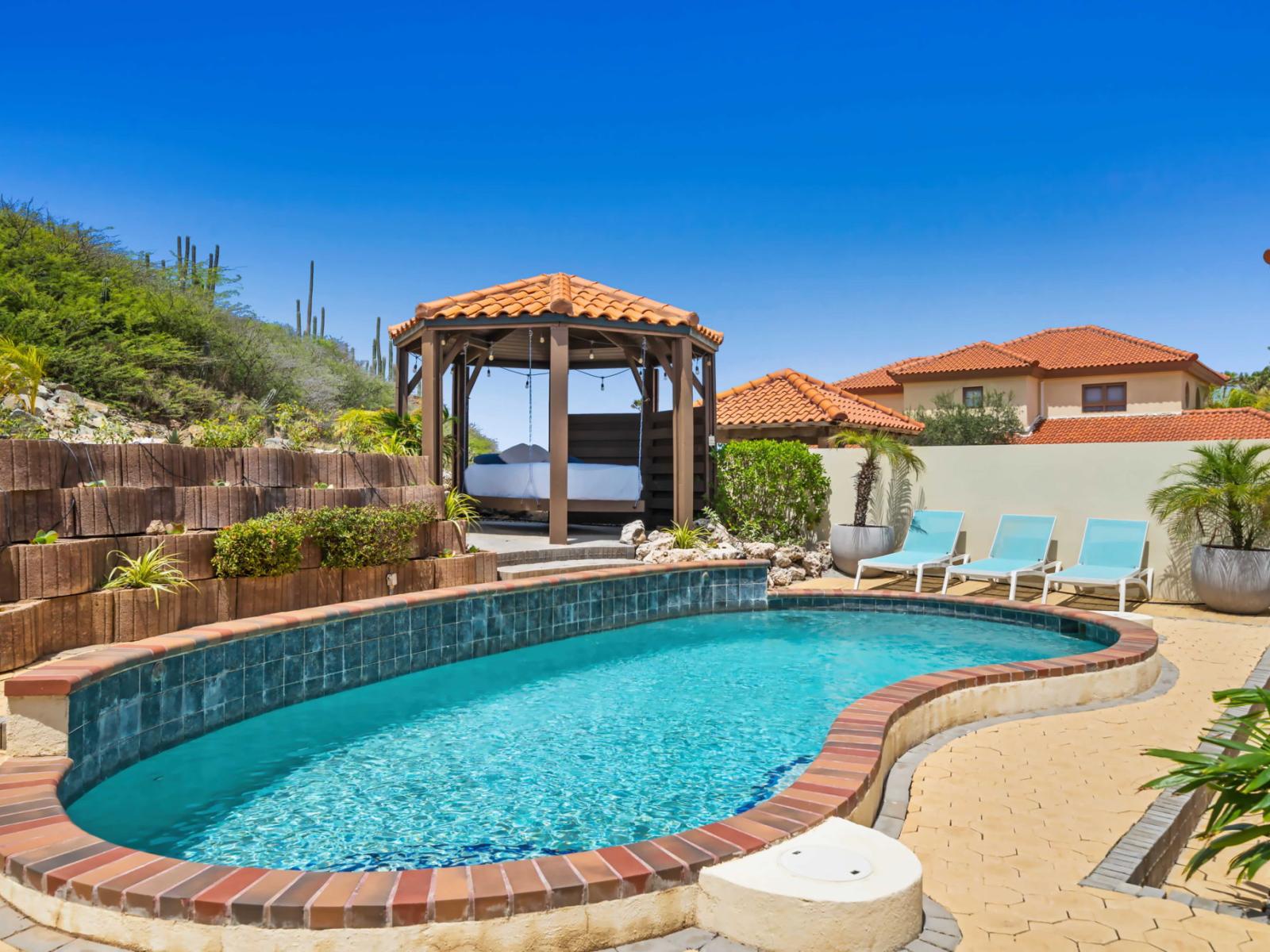 The pool's design, with its curved edges and tile accents, enhances the overall aesthetic appeal - The surrounding landscape includes lush greenery and desert plants, creating a serene environment - Covered gazebos provide shaded areas for lounging