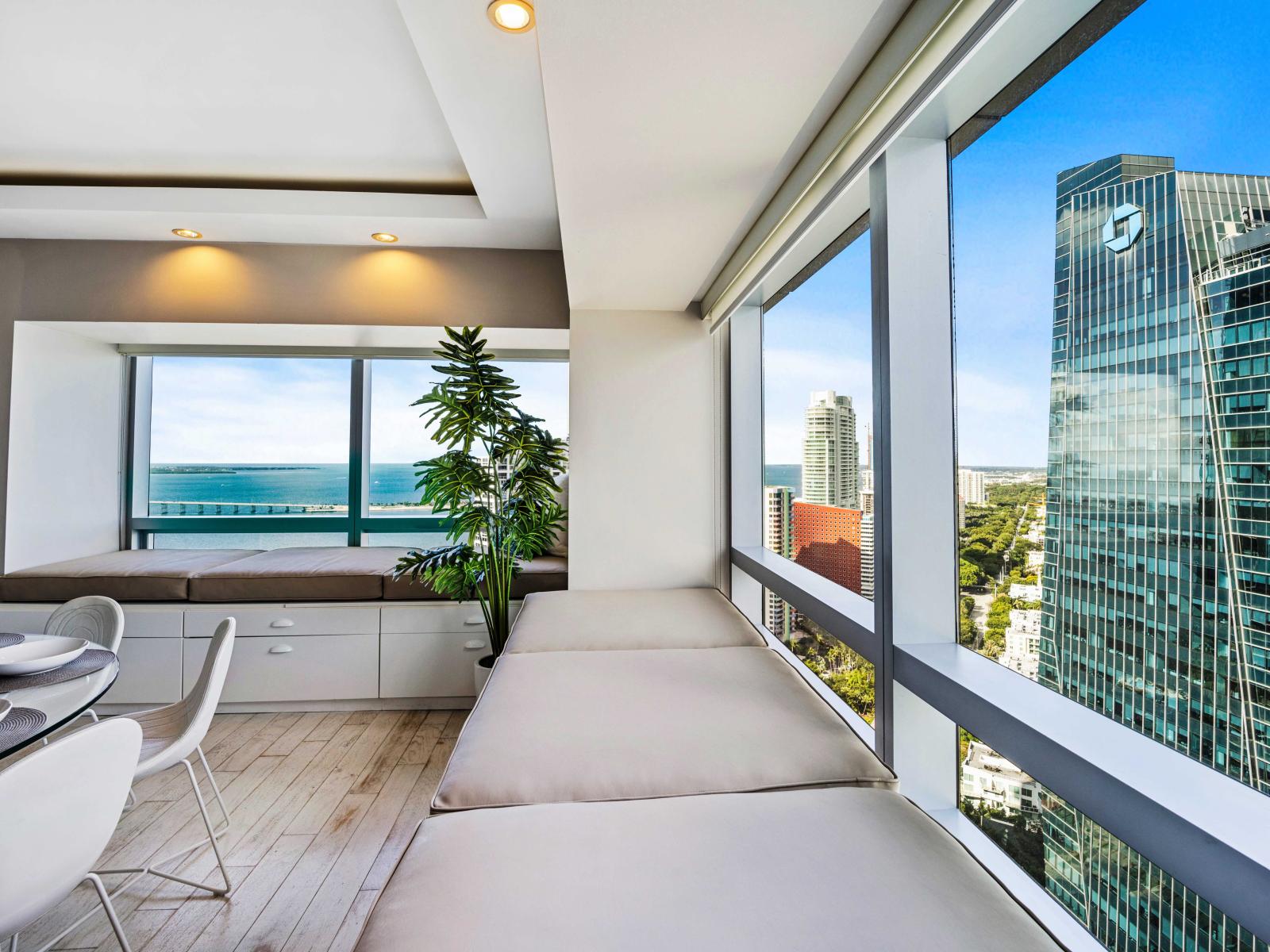 - Cozy window seating area with panoramic city and ocean views perfect for relaxation -  Airy dining space adjacent to large windows enhancing the dining experience -  Modern decor with comfortable seating creating a serene atmosphere for your stay