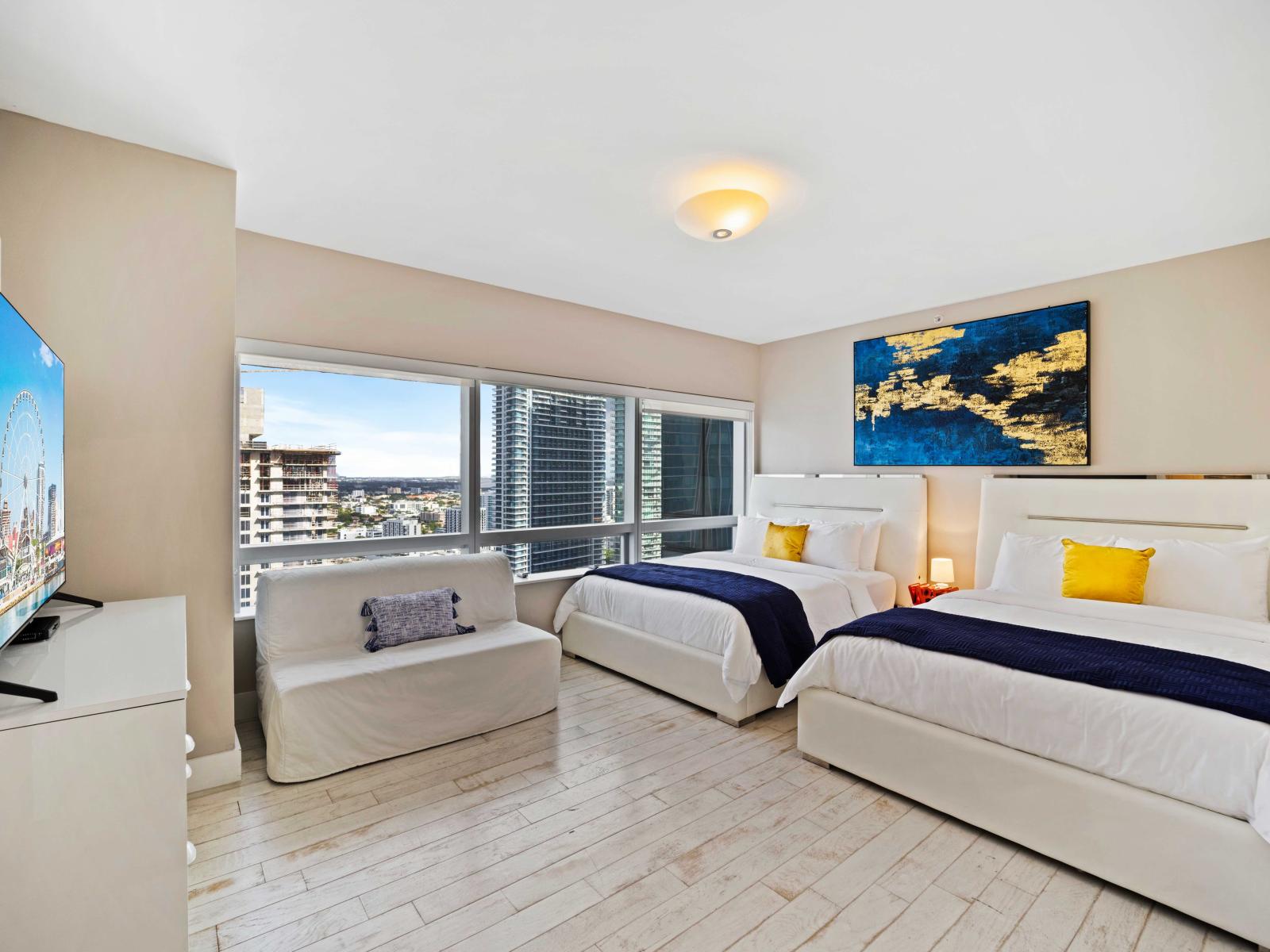 - Spacious bedroom featuring two comfortable double beds with plush linens - Large smart TV and cozy seating area, perfect for relaxing and unwinding - Modern decor with vibrant artwork, and large windows offering a stunning city view