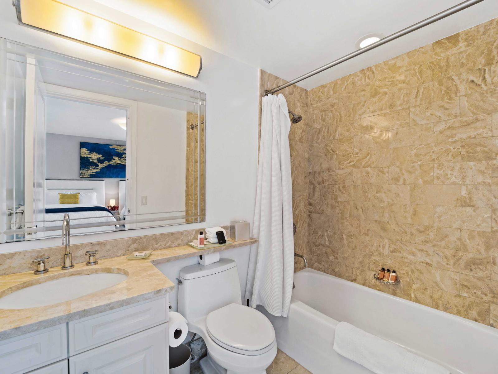 - Polished bathroom featuring spacious vanity with modern fixtures - Elegant design with a tub-shower combo and stylish tile work for a relaxing experience - Well-lit space with a large mirror and plush towels providing a comfortable atmosphere